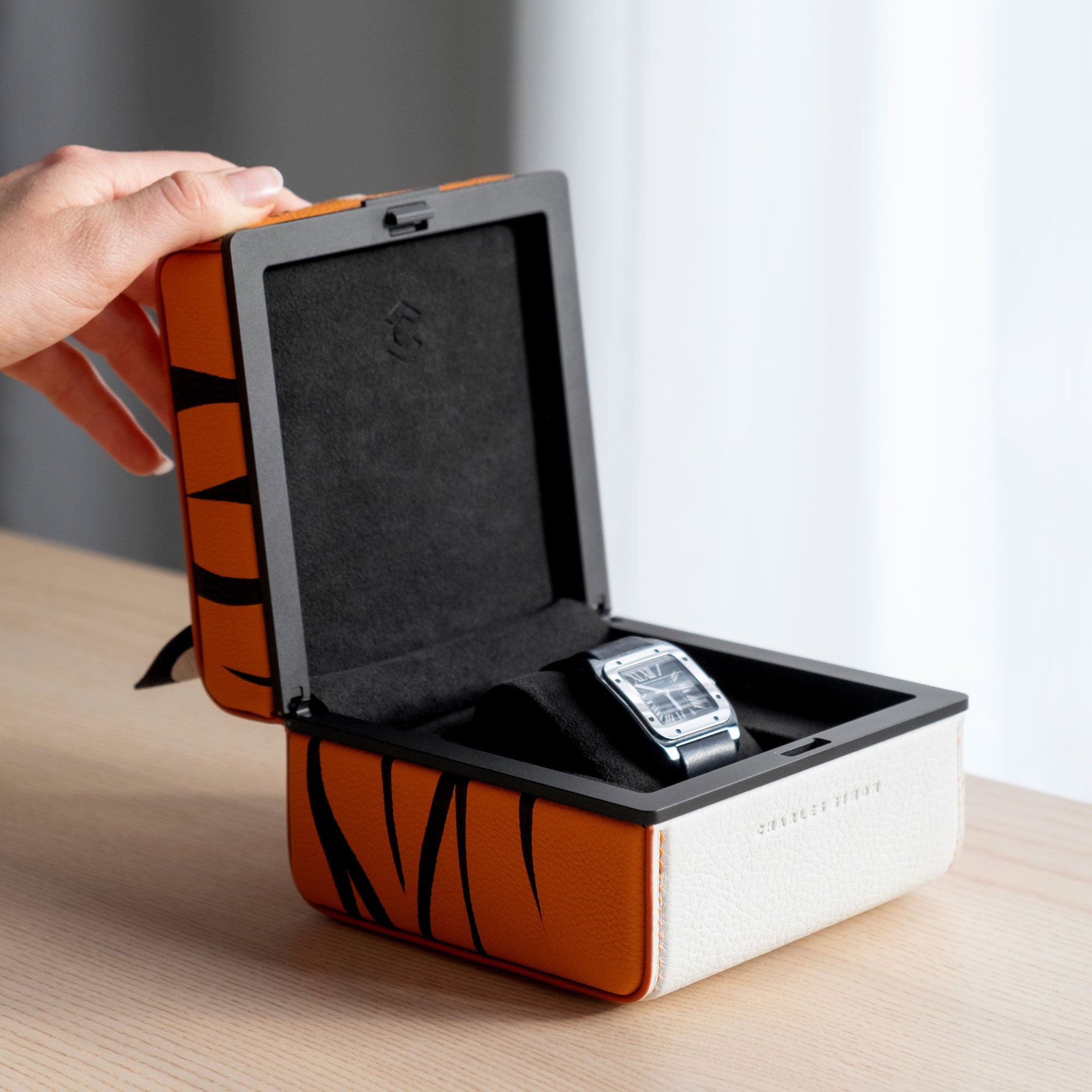 Lifestyle photo of hand opening Tiger Eaton 1 special edition watch case showcasing the bold tiger pattern handmade from French leather. The watch case is storing one watch on a black watch cushion.