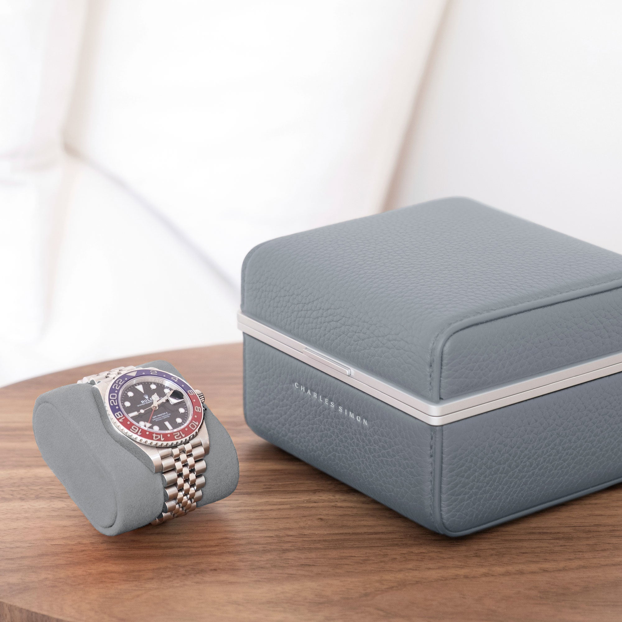 Lifestyle photo of Eaton 1 Watch case in cloud grey leather and fog grey Alcantara interior. Rolex Pepsi is placed on removable Alcantara cushion next to closed luxury watch case.