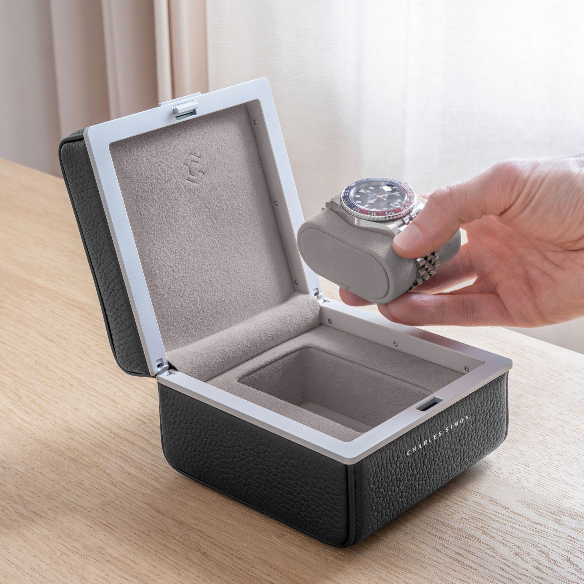 Lifestyle photo of open Eaton 1 Watch case in graphite leather and sea sand Alcantara interior. Man is taking Rolex Pepsi luxury watch placed on removable watch cushion from the handmade watch case.