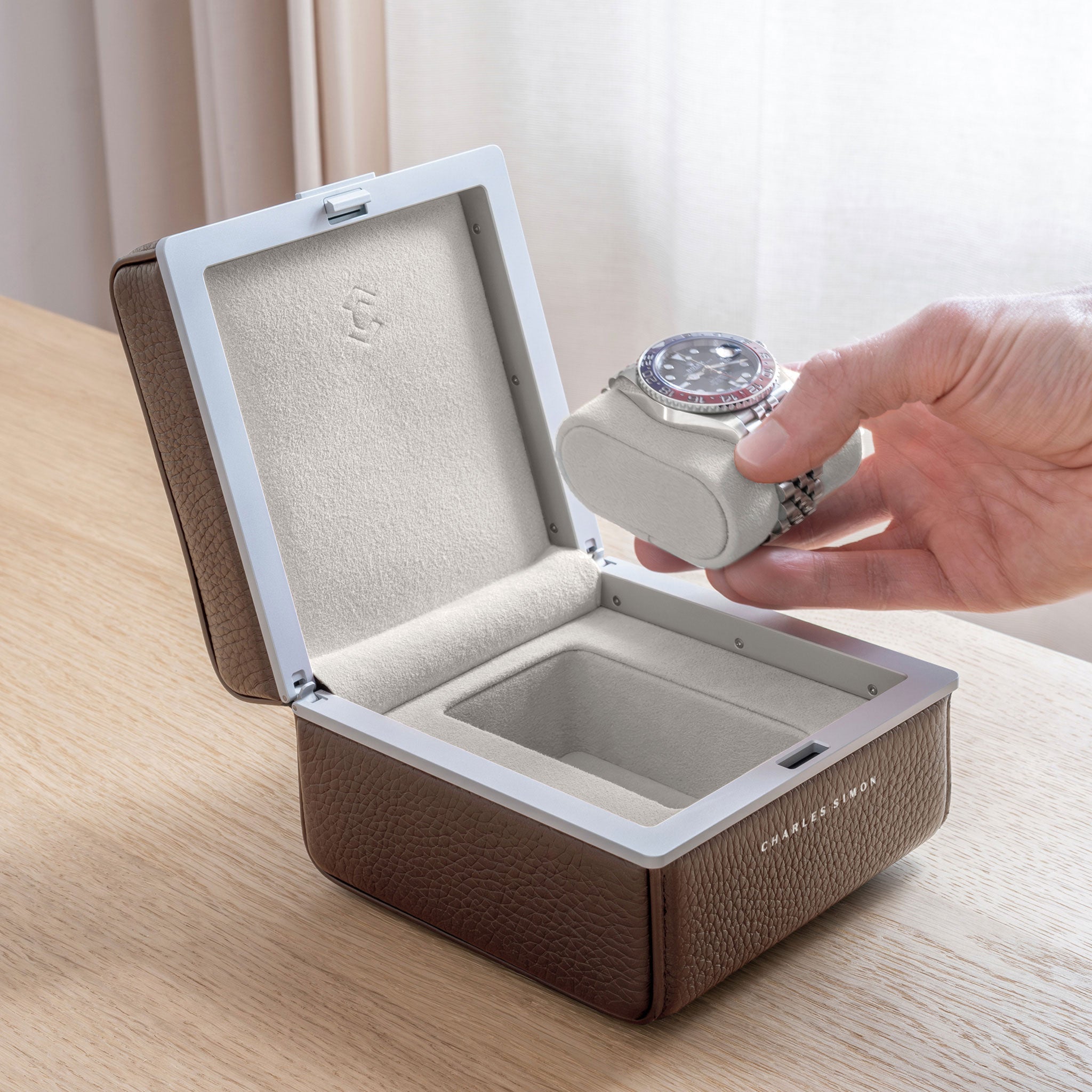 Lifestyle photo of open Eaton 1 Watch case in tan leather and eggshell Alcantara interior. Man is taking Rolex Pepsi luxury watch placed on removable watch cushion