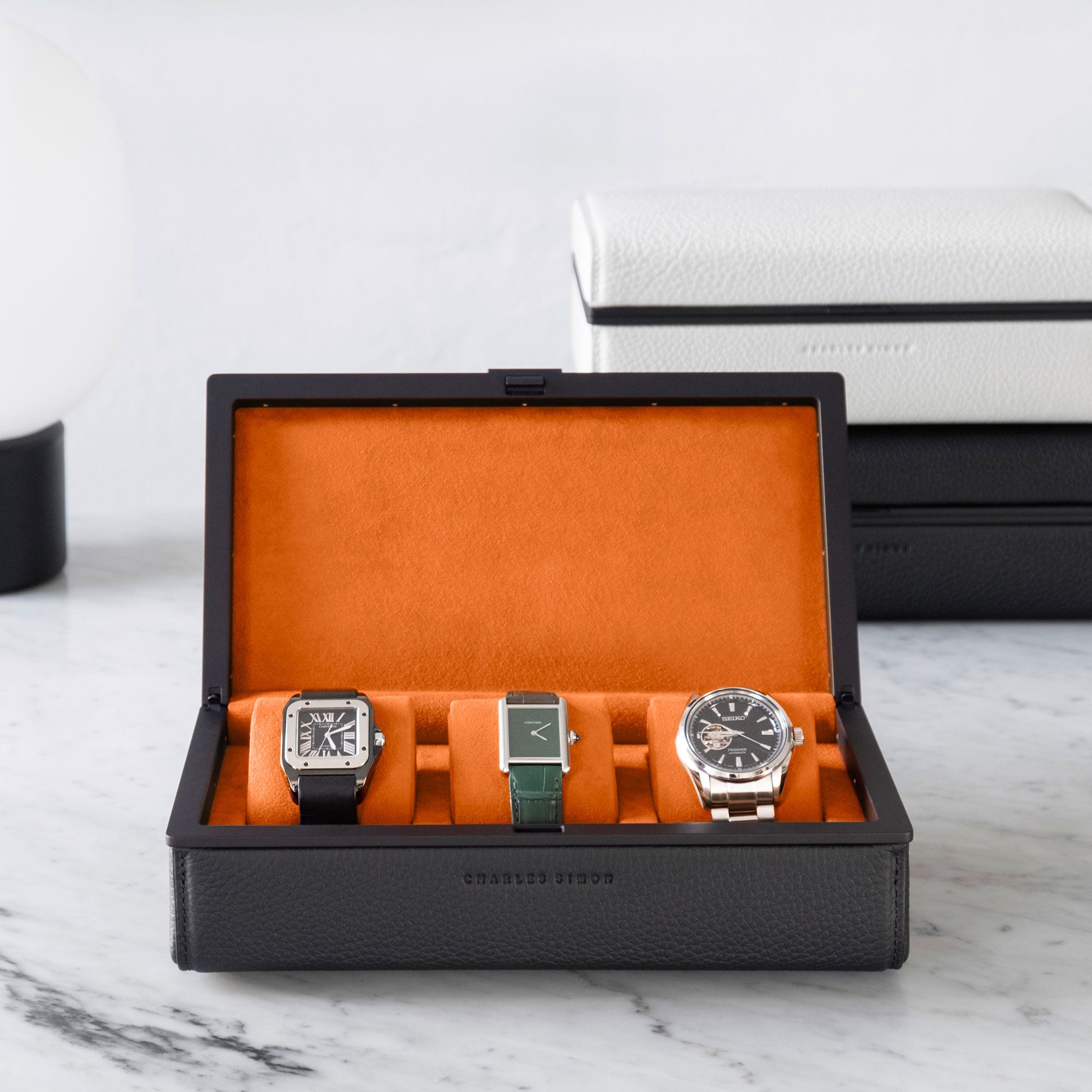 Lifestyle shot of open Eaton 3 Watch case in black leather with black anodized aluminum and soft papaya Alcantara interior holding 3 luxury watches including Cartier