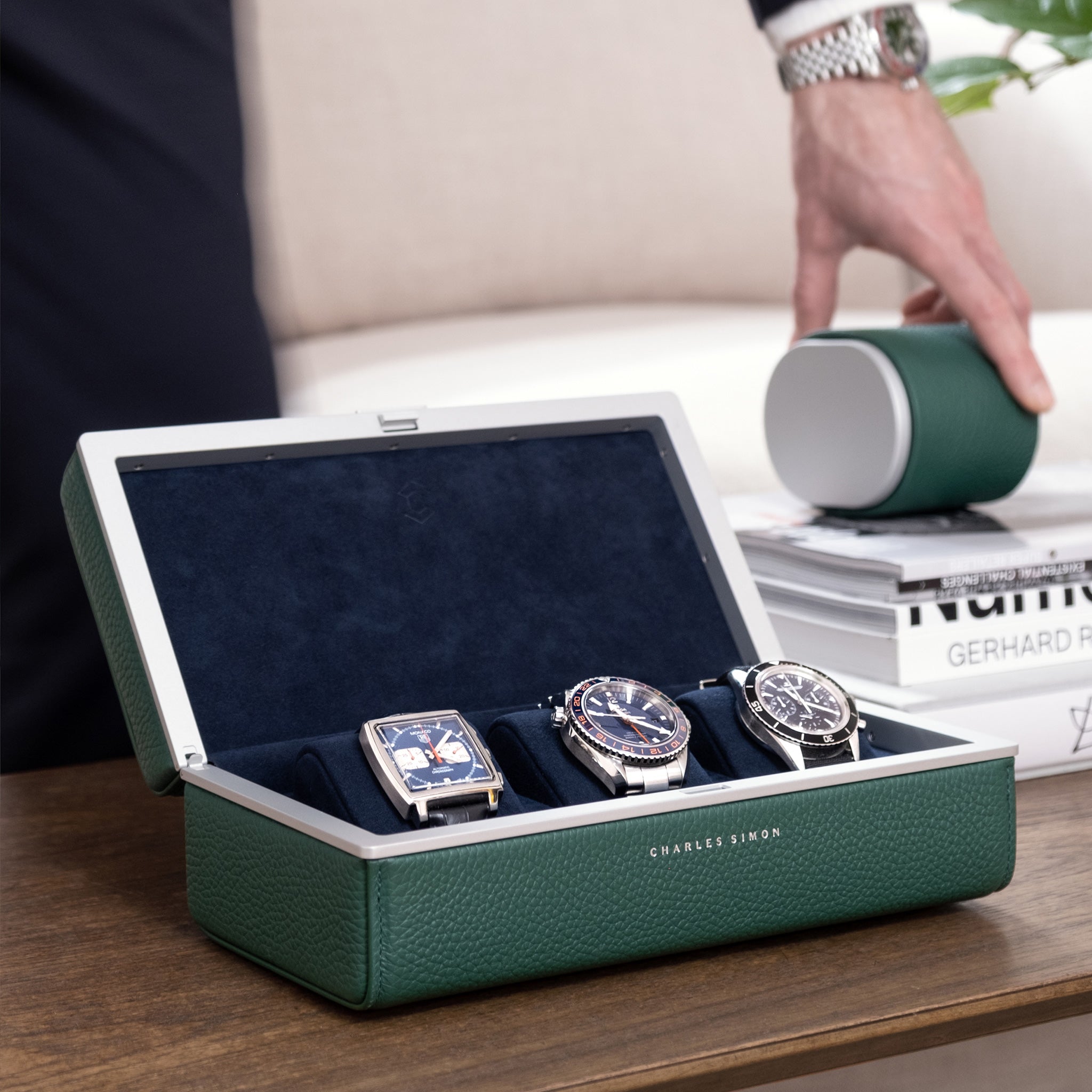 Lifestyle photo of open emerald Eaton 3 Watch case for a watch collection of up to 3 watches. Man is grabbing emerald Theo Watch roll in the background.