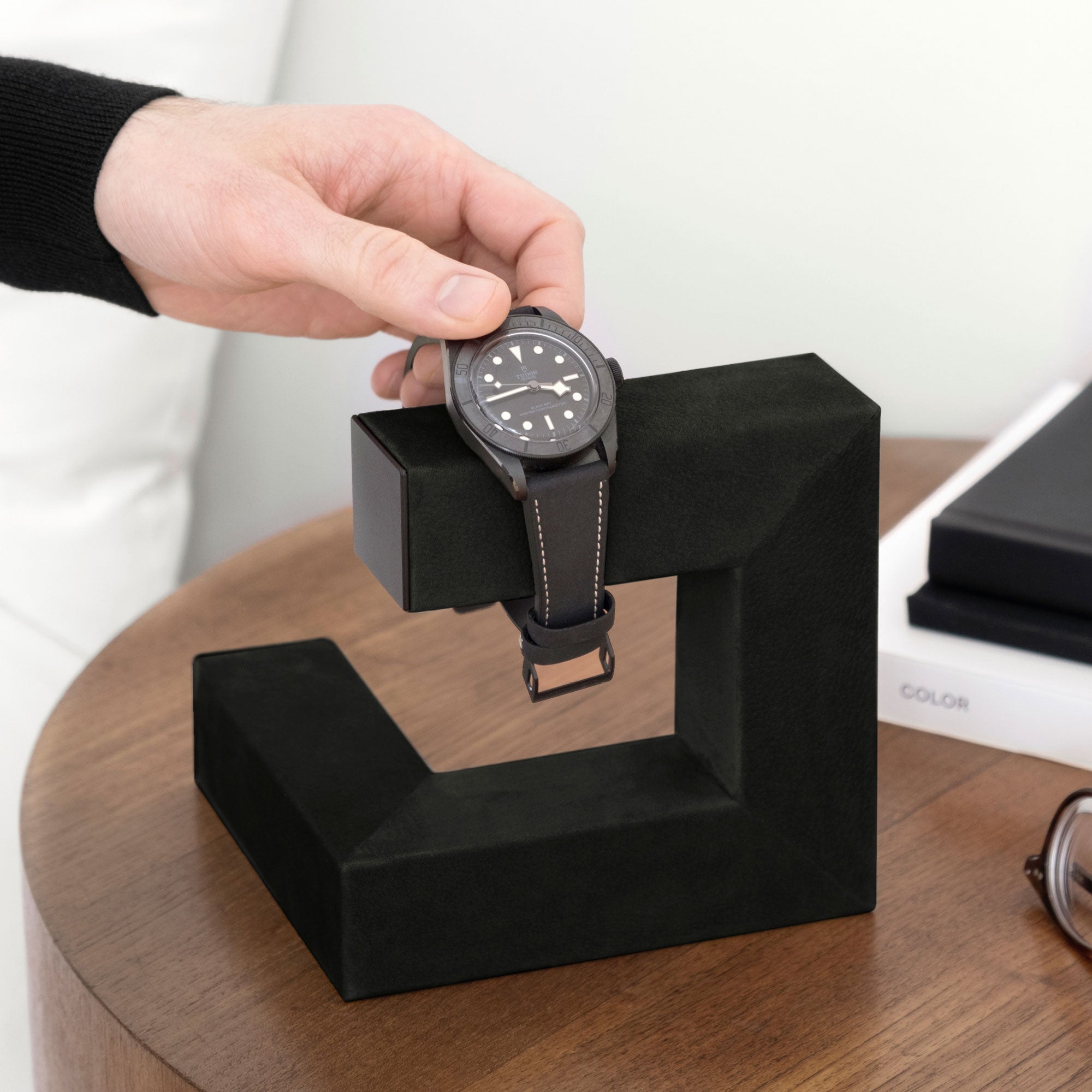 Lifestyle photo of man taking watch from all black watch stand inspired by contemporary art