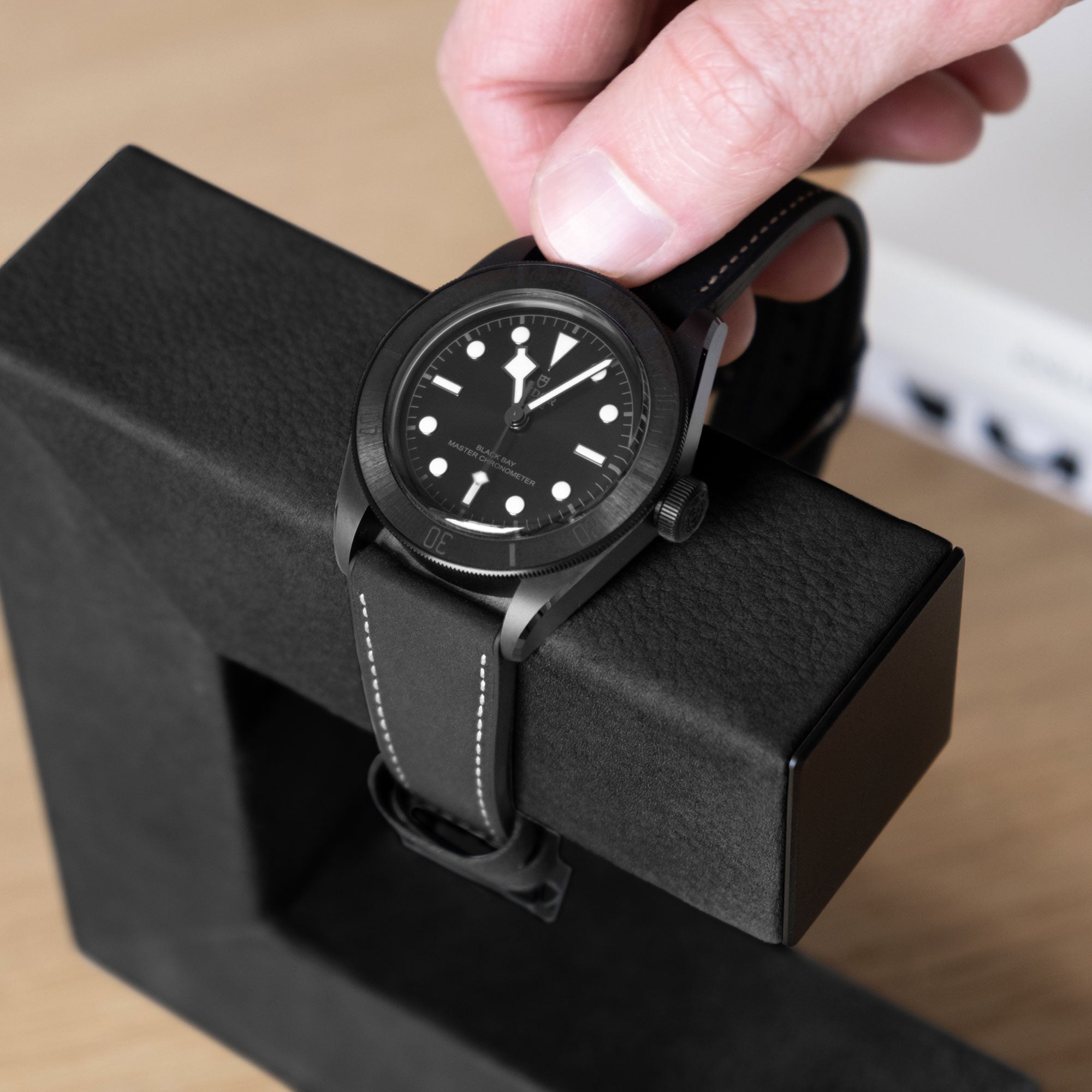 Detail shot of man taking his all black watch from his all black Hudson Watch stand 