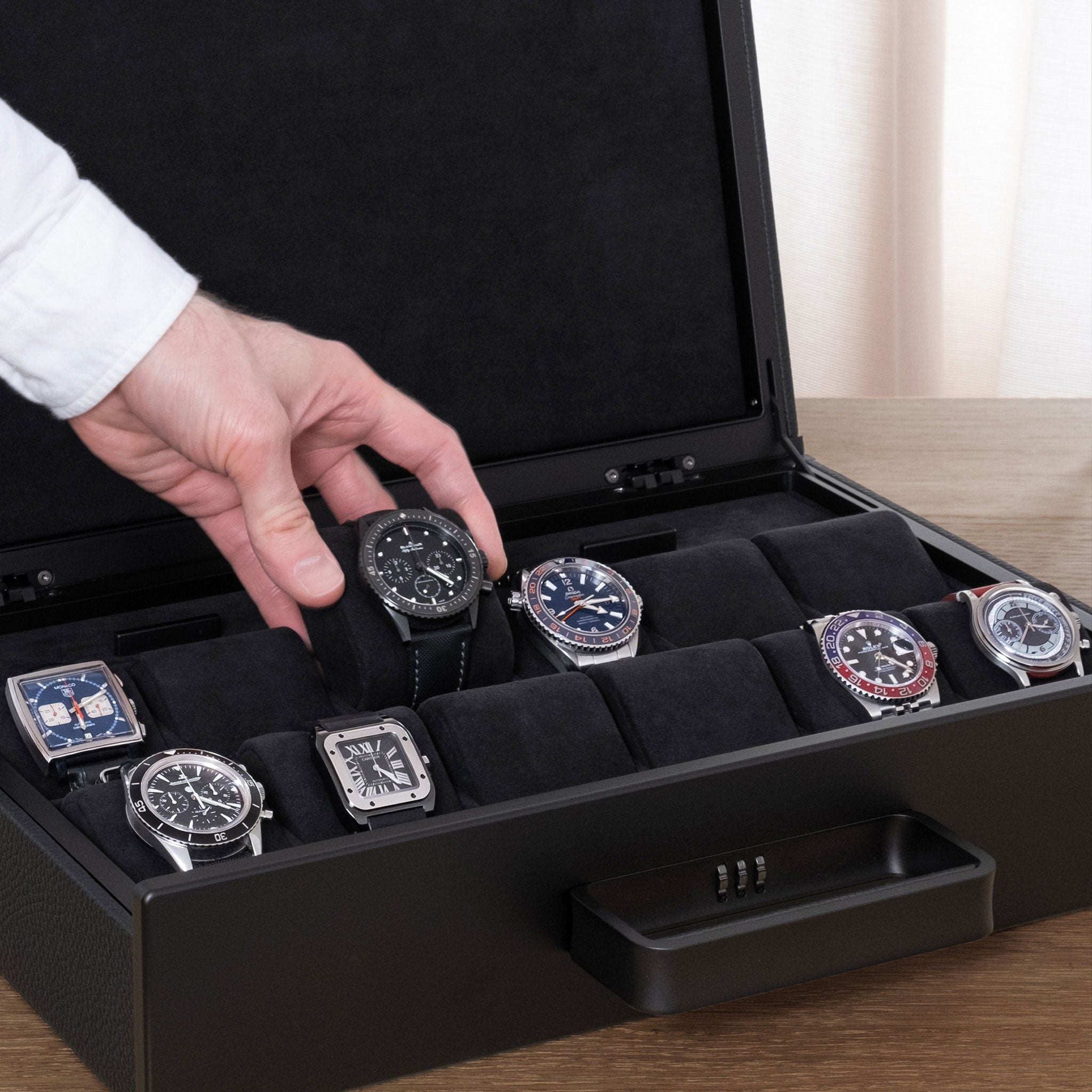 Lifestyle shot of open Mackenzie 12 Watch briefcase in all black carbon fiber and aluminum casing, black leather and soft black Alcantara made by hand filled with luxury watches including Rolex, Blancpain and Omega