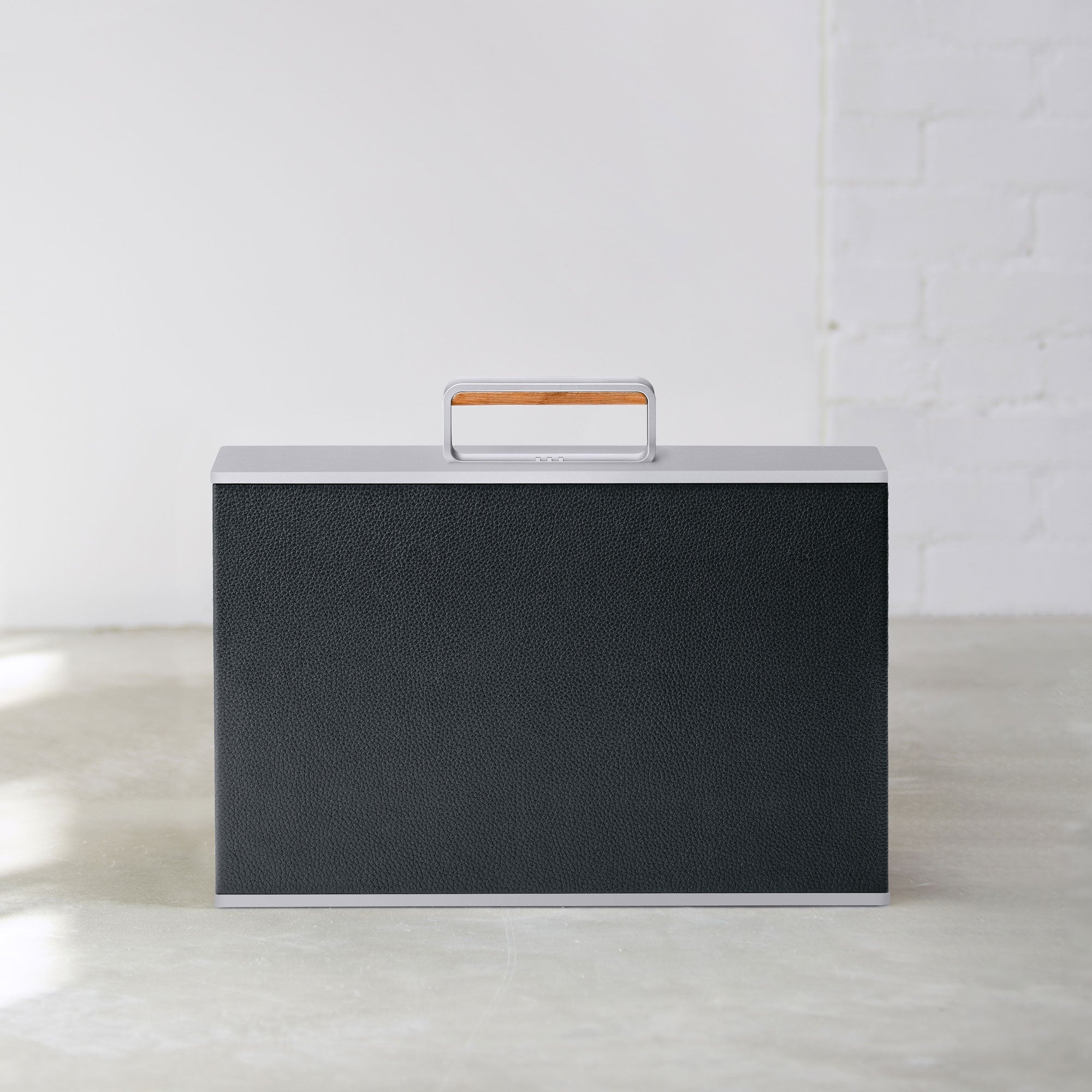 Lifestyle photo of Mackenzie Watch briefcase in black leather, grey aluminum and a wood handle detail. Handmade in Canada.