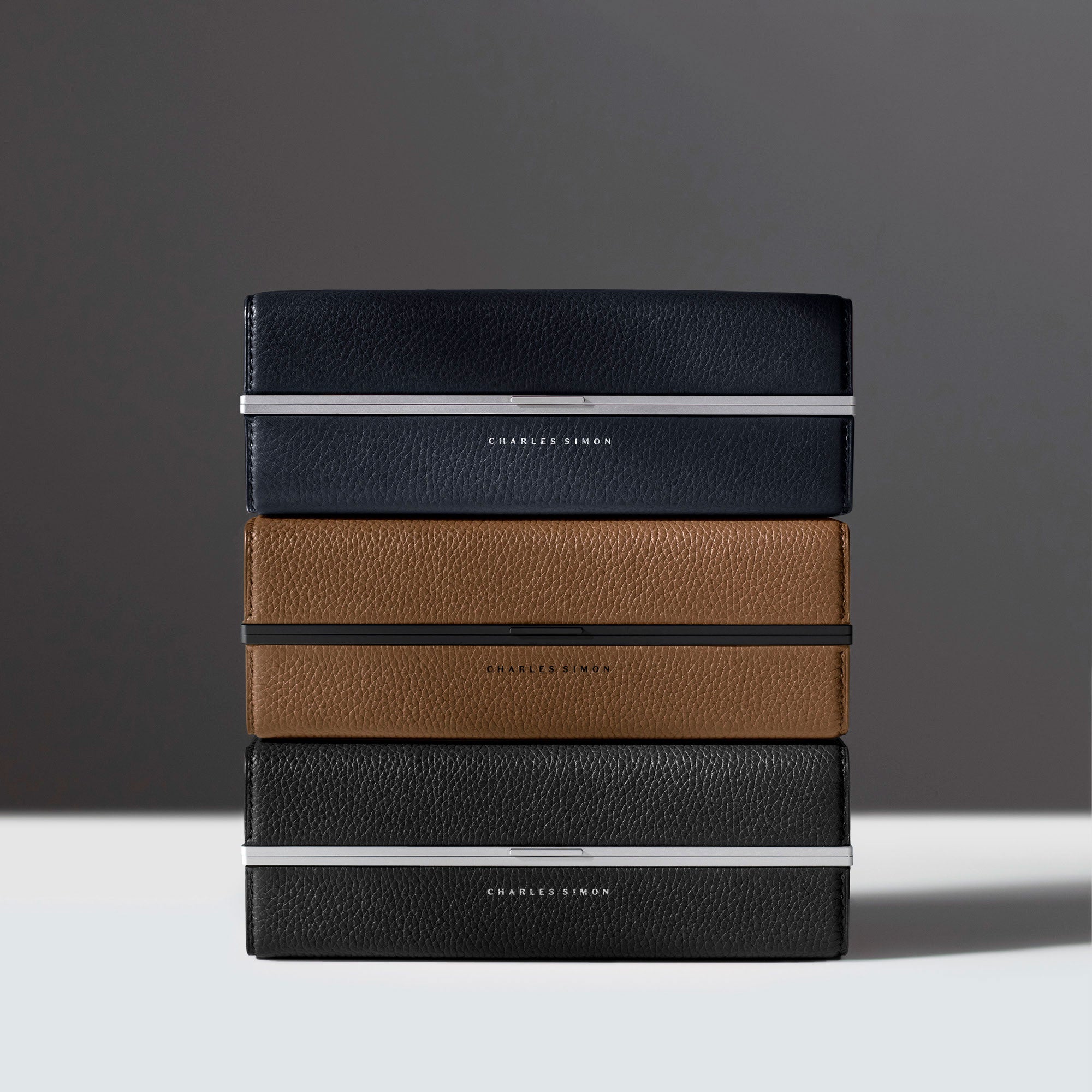 Lifestyle photo of three stacked Moraine Toiletry bags featuring sleek, timeless design. Handmade from premium French leather and anodized aluinum.