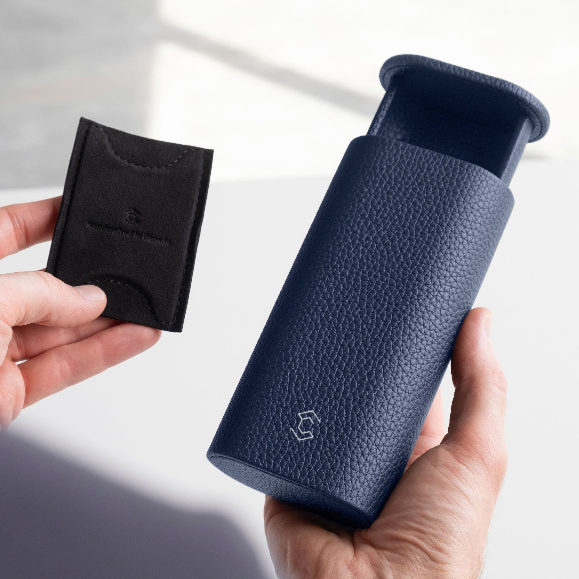 Man holding half open sapphire leather watch roll in one hand and the removable card insert to keep the watch in place in the left hand. By Charles Simon.