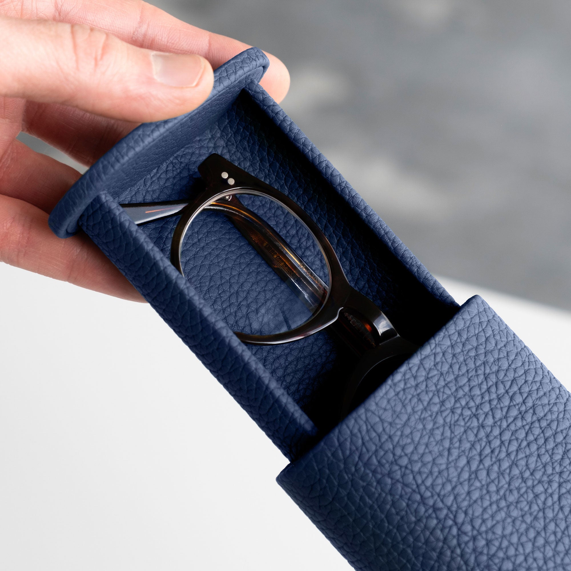 Man opening sapphire leather Oscar Tall Watch roll holding a pair of elegant glasses