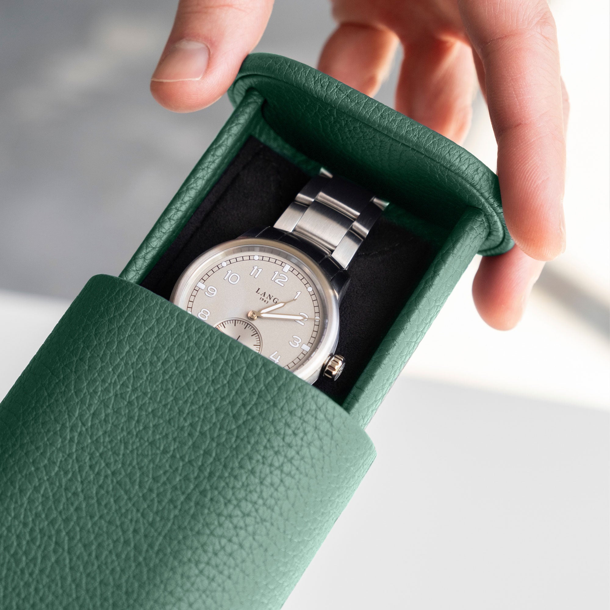 Man opening his emerald green leather Oscar 1 Travel Watch roll revealing the watch with a metal bracelet which is stored inside.