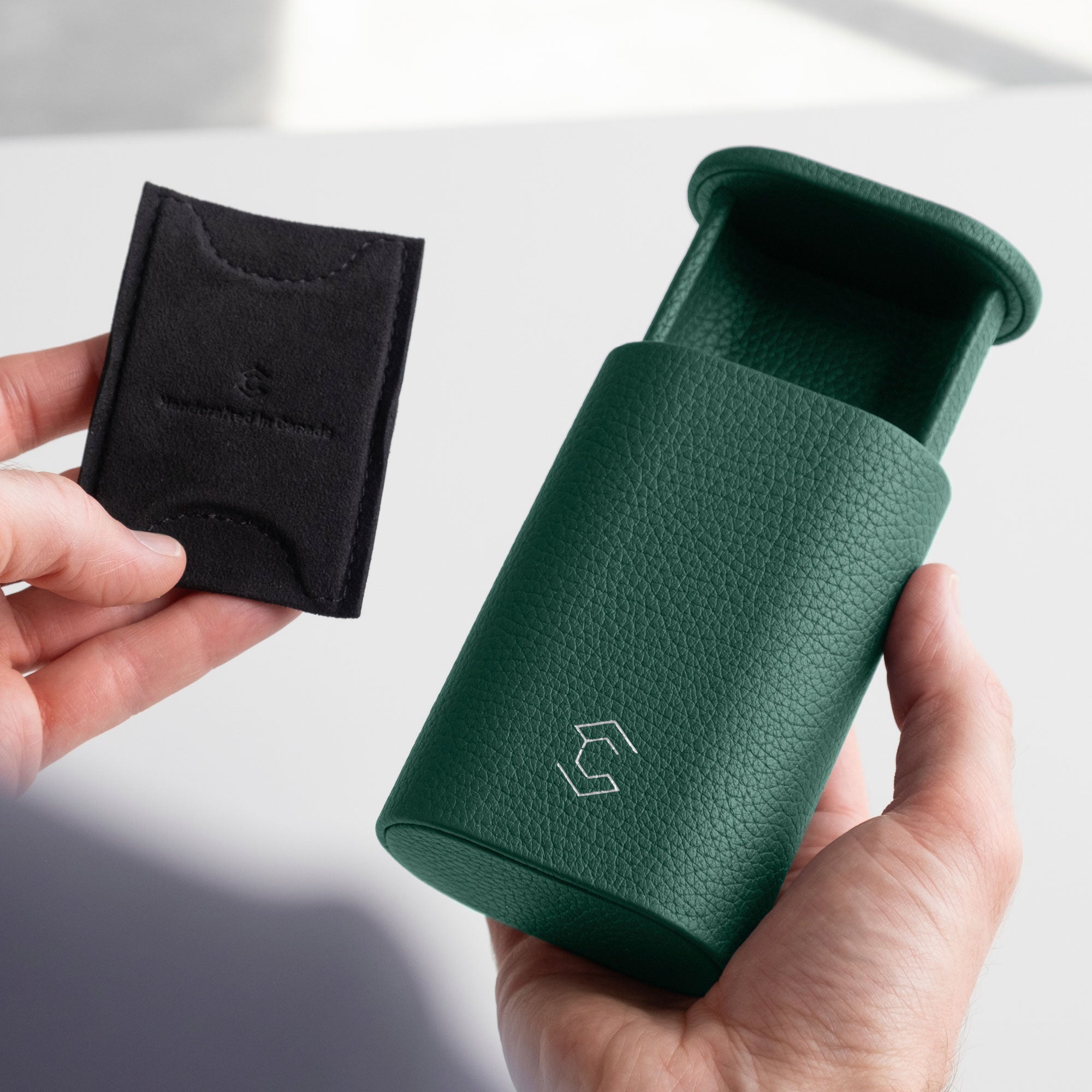 Man holding open emerald leather Oscar travel watch roll in one hand and removable card insert to keep the watch secure within the watch roll in the other hand.