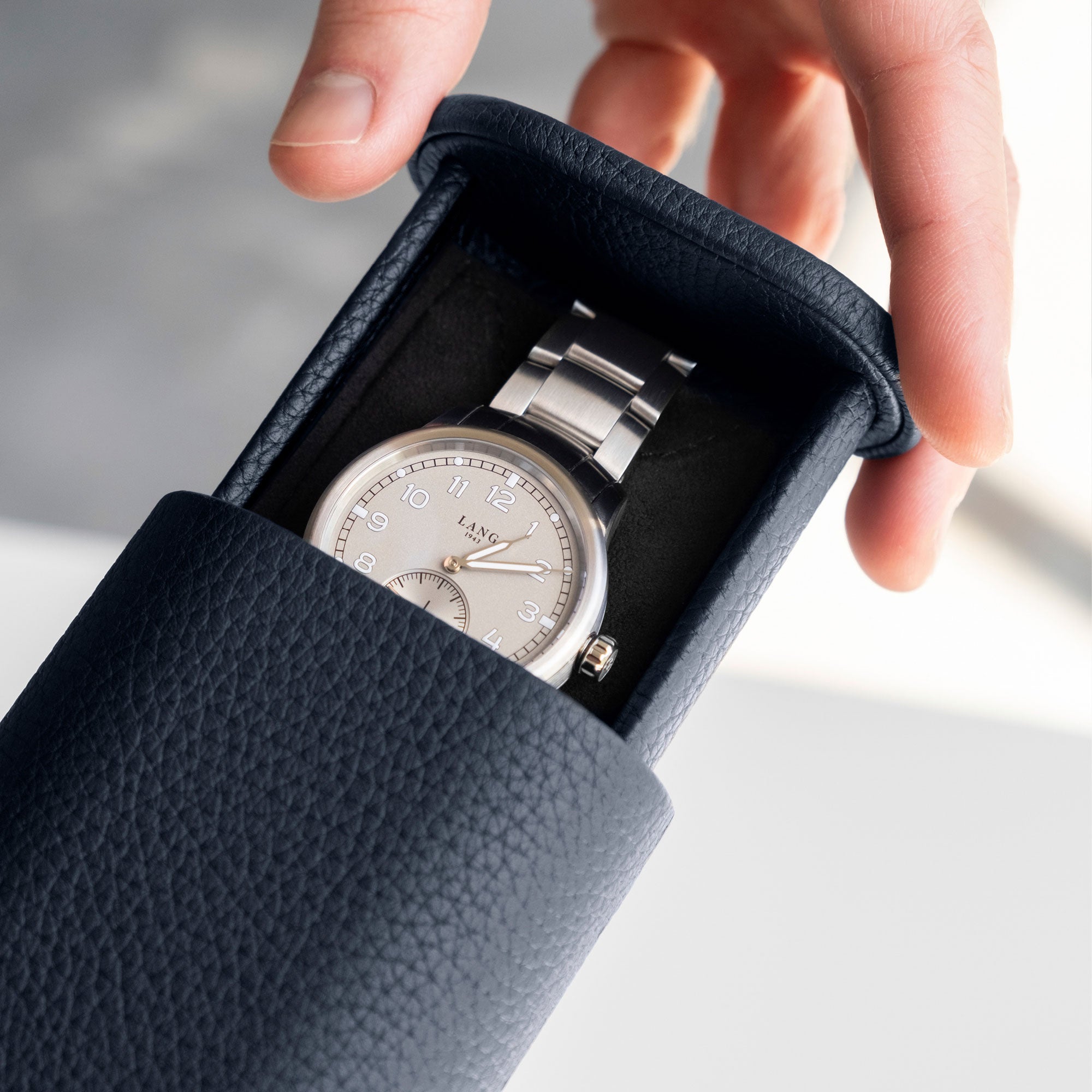 Closeup detail photo of man opening his marine french leather Oscar 1 Watch roll that holds one watch with a metal bracelet