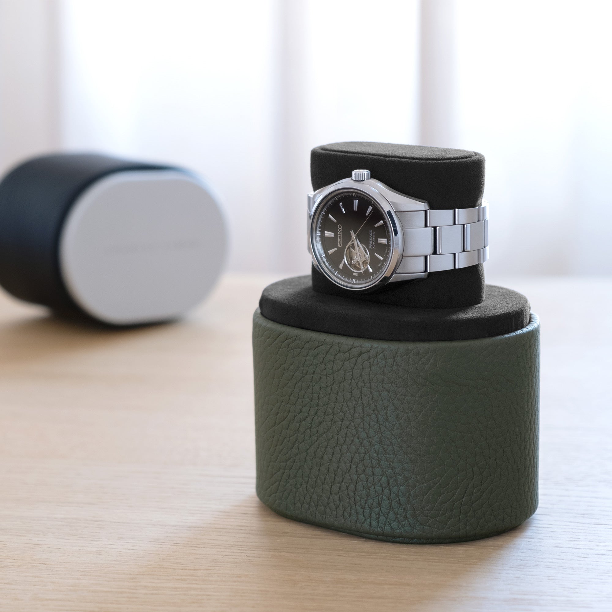 Lifestyle shot of open Theo leather watch roll in khaki, black anodized aluminum, and black interior in convenient portable watch stand position holding one watch