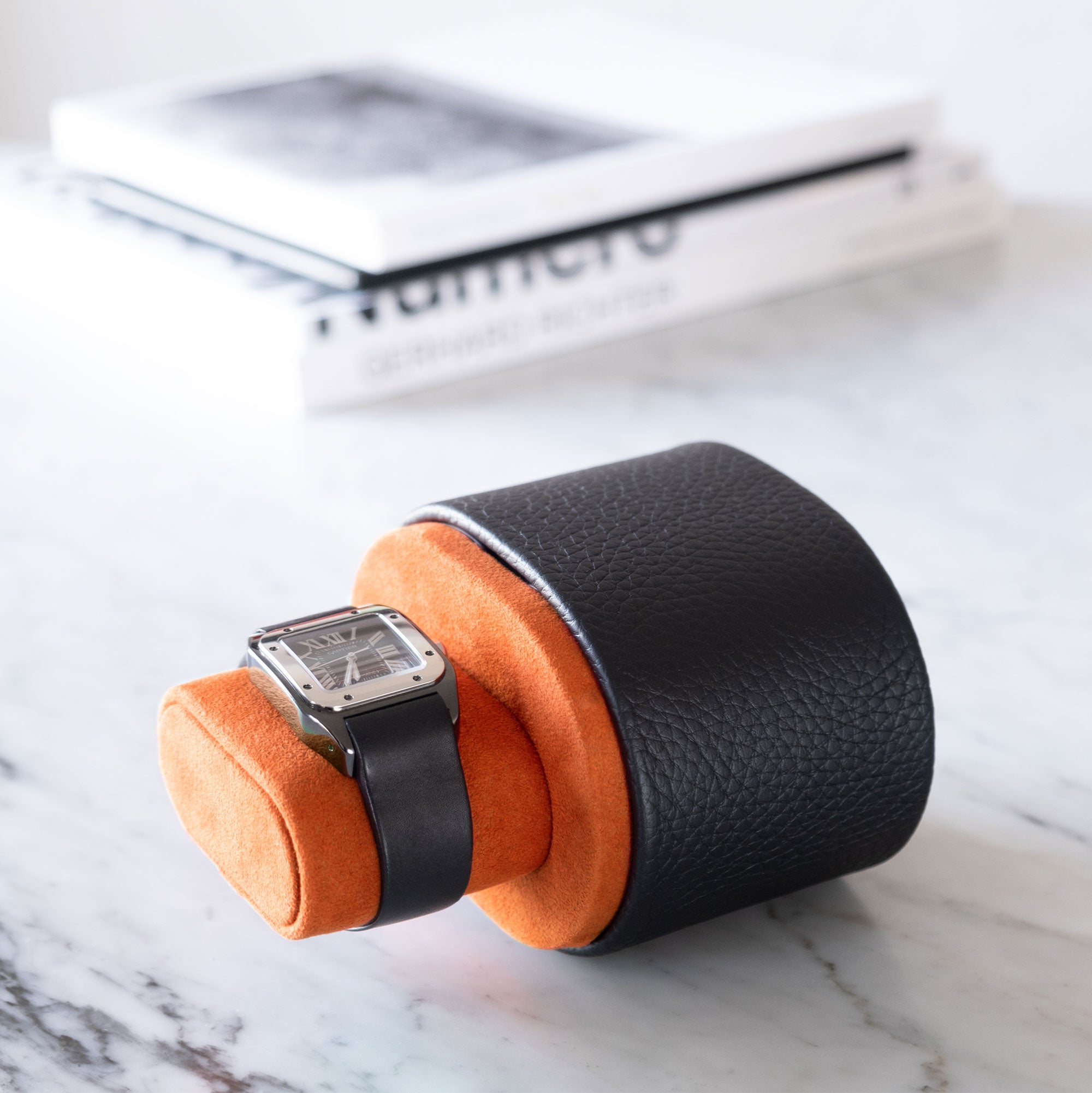 Lifestyle shot of open black leather Theo watch roll holding one watch on Papaya Alcantara watch cushion.