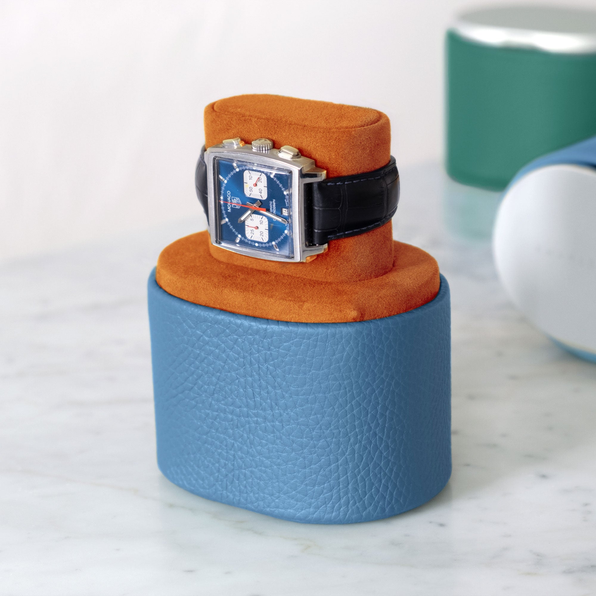 Lifestyle shot of handmade Theo watch roll in sky blue leather and Papaya interior holding Tag Heuer Monaco luxury watch