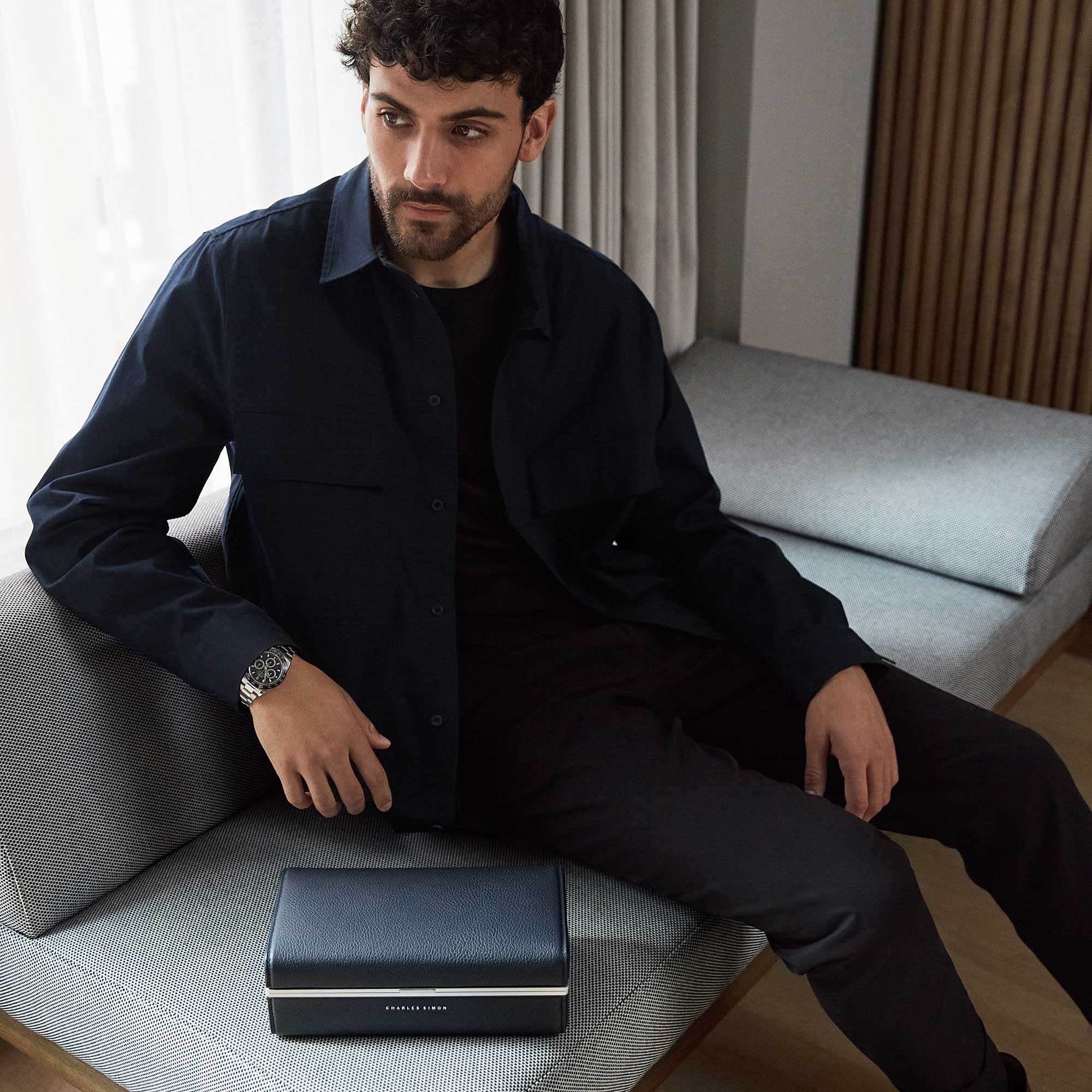 Lifestyle shot of man in minimalist clothing wearing a Rolex luxury men's watch sitting next to Eaton 3 watch case in marine young bull leather