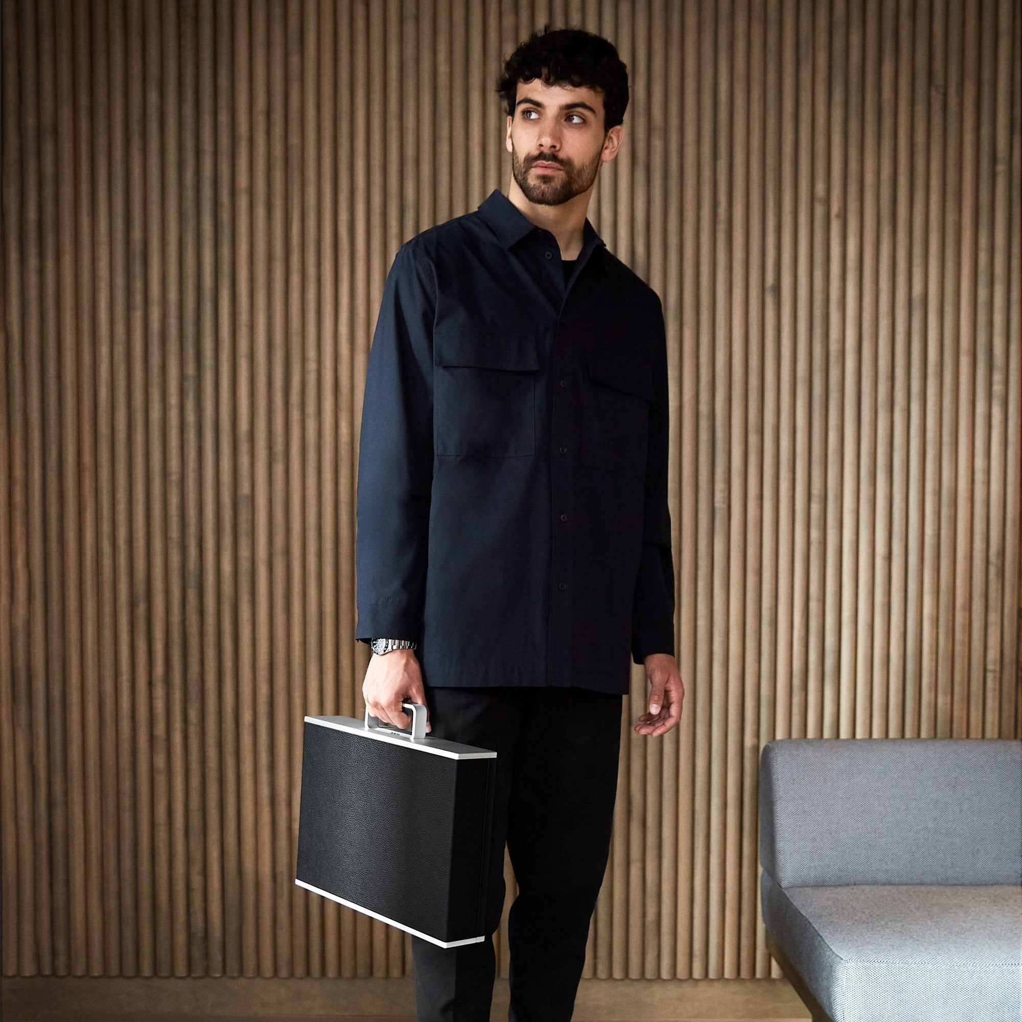 Lifestyle shot of young man wearing navy minimalist suit holding the handmade Charles Simon Mackenzie watch case in black