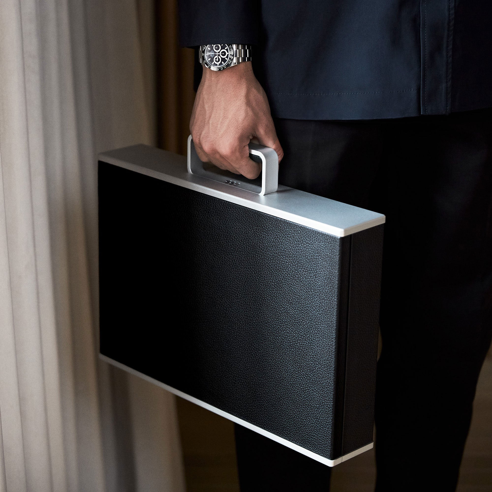 Man wearing Rolex watch on wrist while holding black Mackenzie Watch case made by hand from young bull leather, aluminum carbon fibre and Alcantara interior