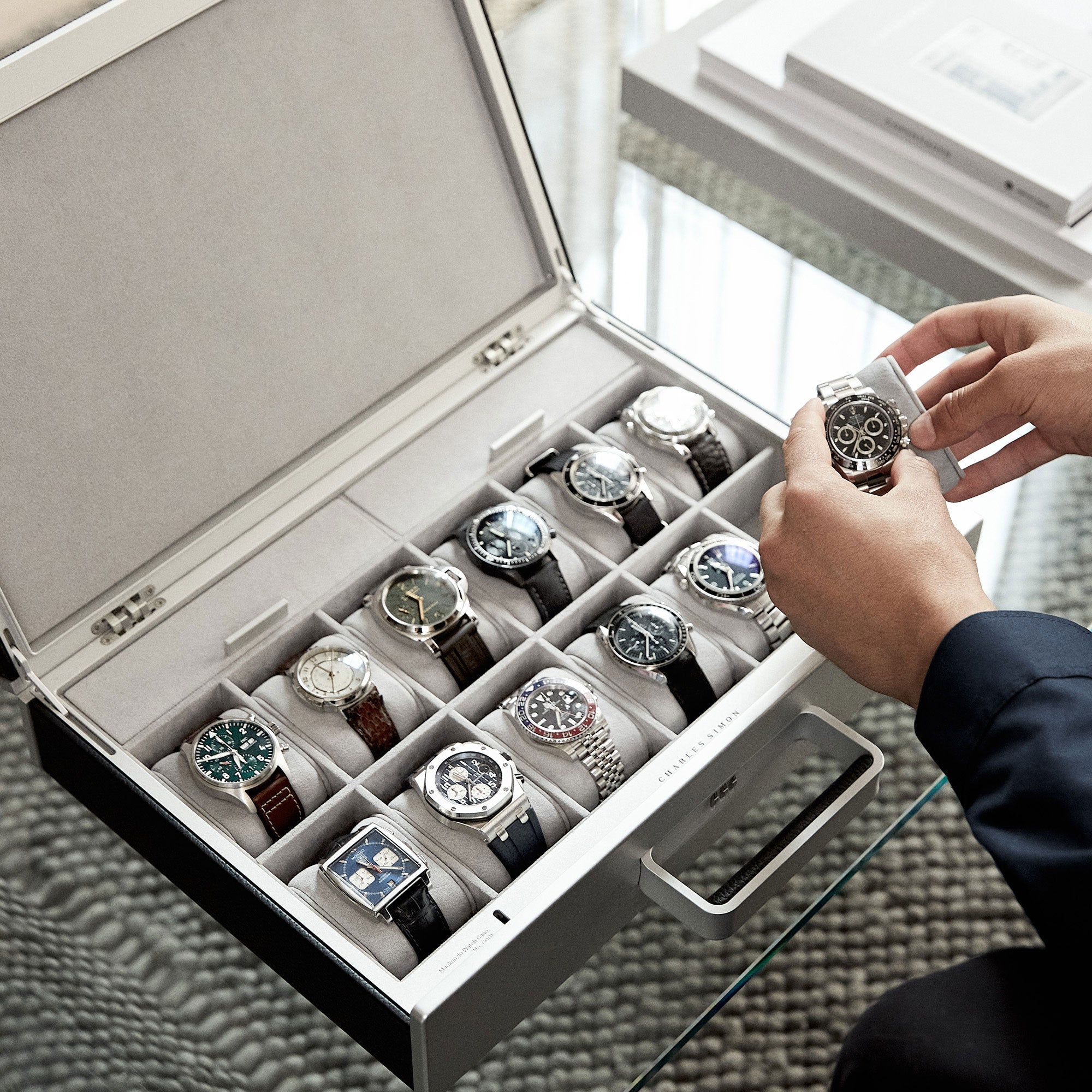 Lifestyle shot of open Mackenzie Watch case 12 by Charles Simon containing a watch collection of 12 luxury watches, including Rolex, Blancpain, Panerai and Jaeger-LeCoultre. Man is holding watch placed on removable Alcantara cushion
