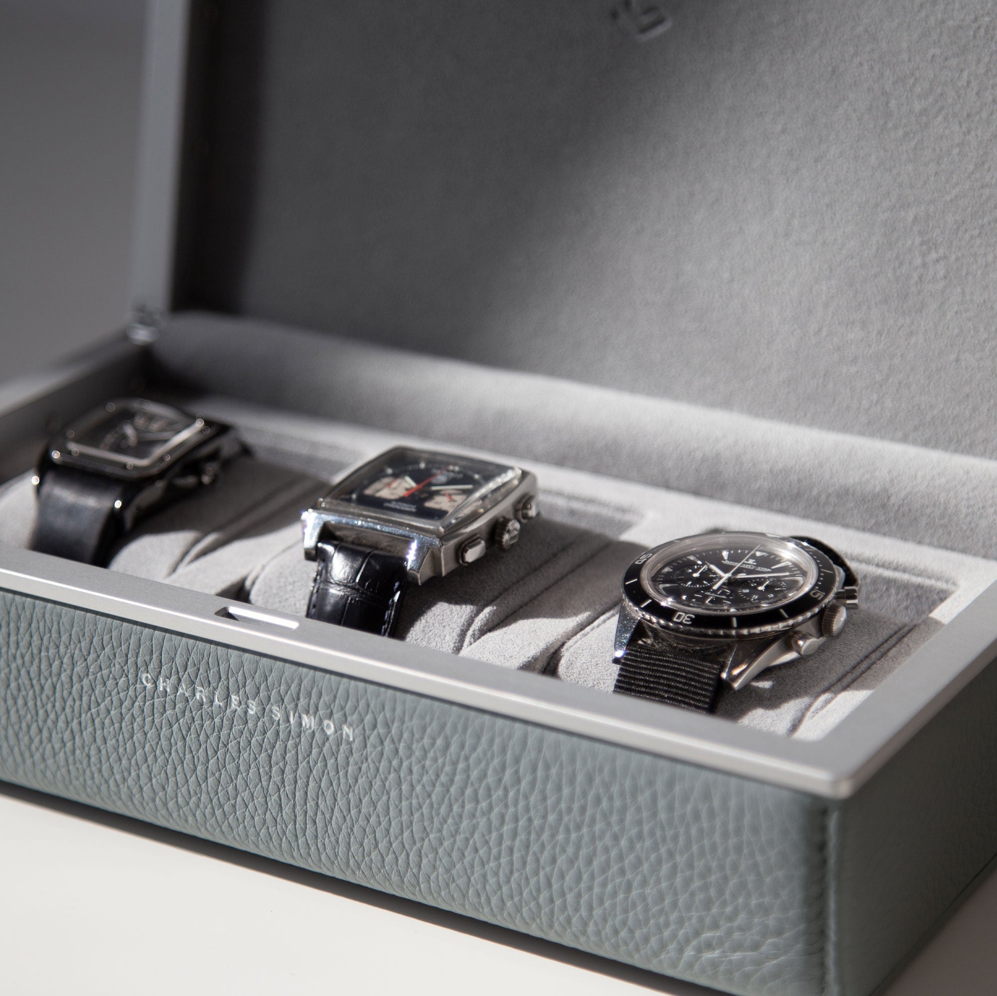 Lifestyle shot of Charles Simon Eaton 3 watch case in cloud grey holding three luxury timepieces placed on milano removable Alcantara cushions