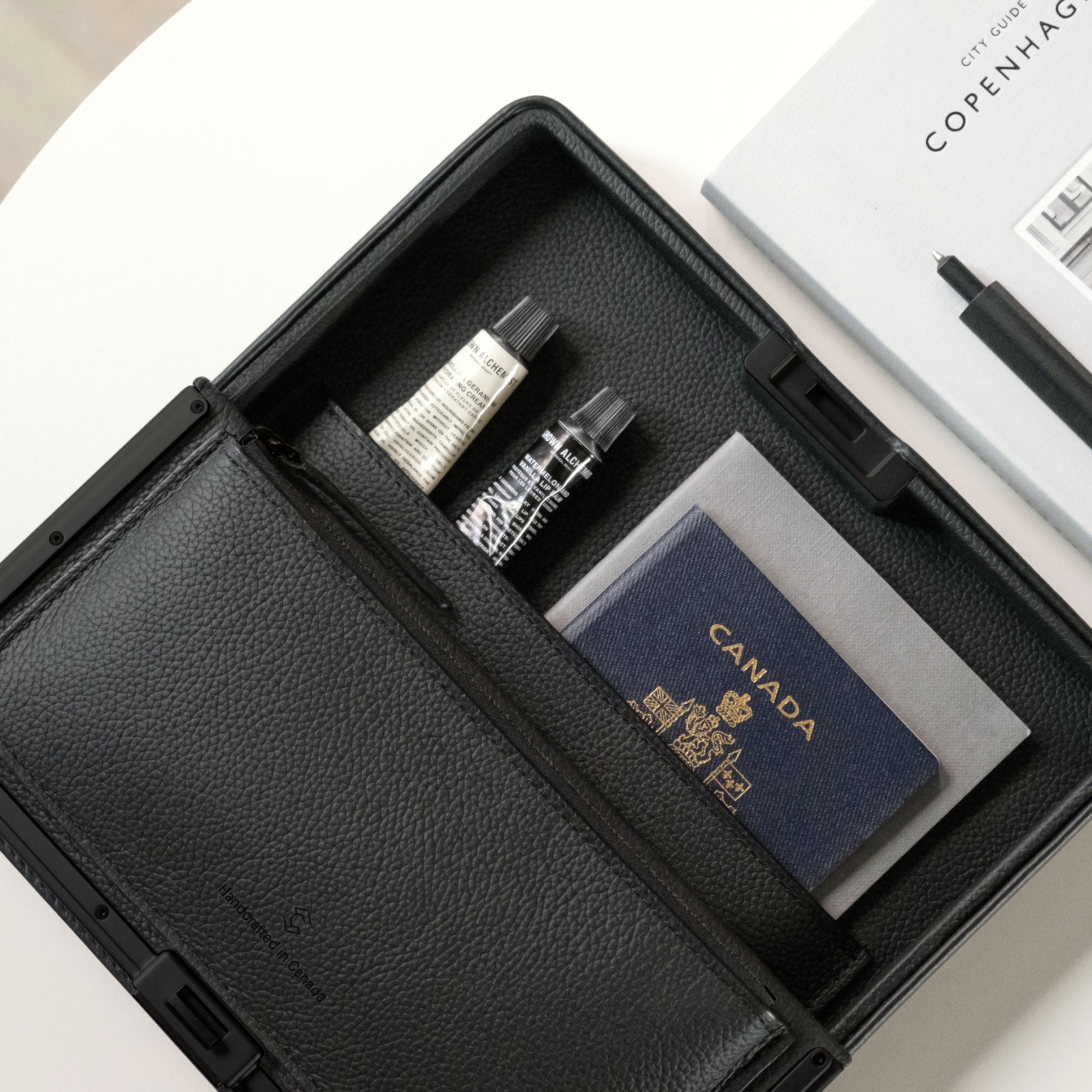 Lifestyle photo of the all black Fraser travel wallet holding travel essentials including a passport, a notebook, hand creams and other necessities.