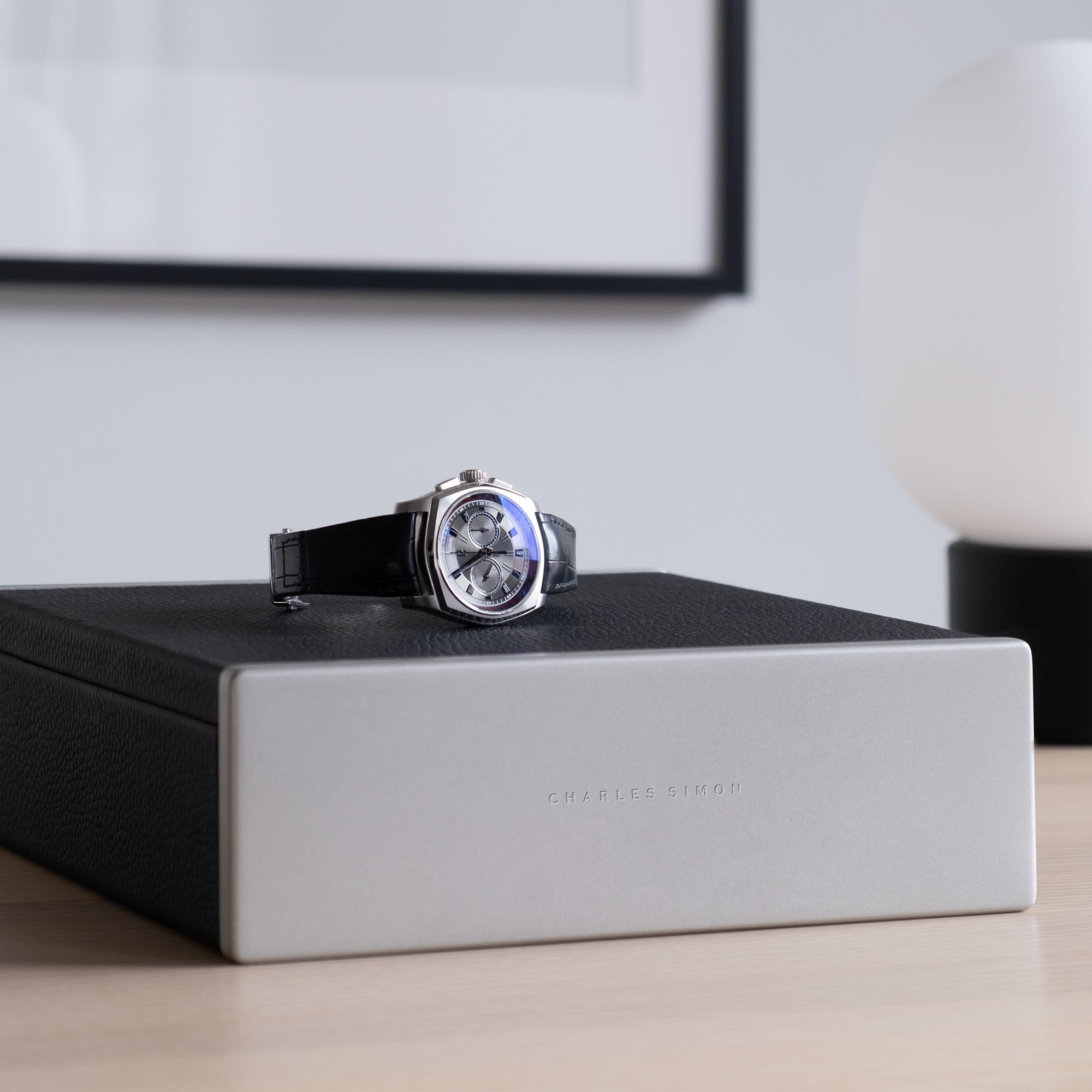 Luxury men's watch placed on top of black leather Spence watch box in modern apartment