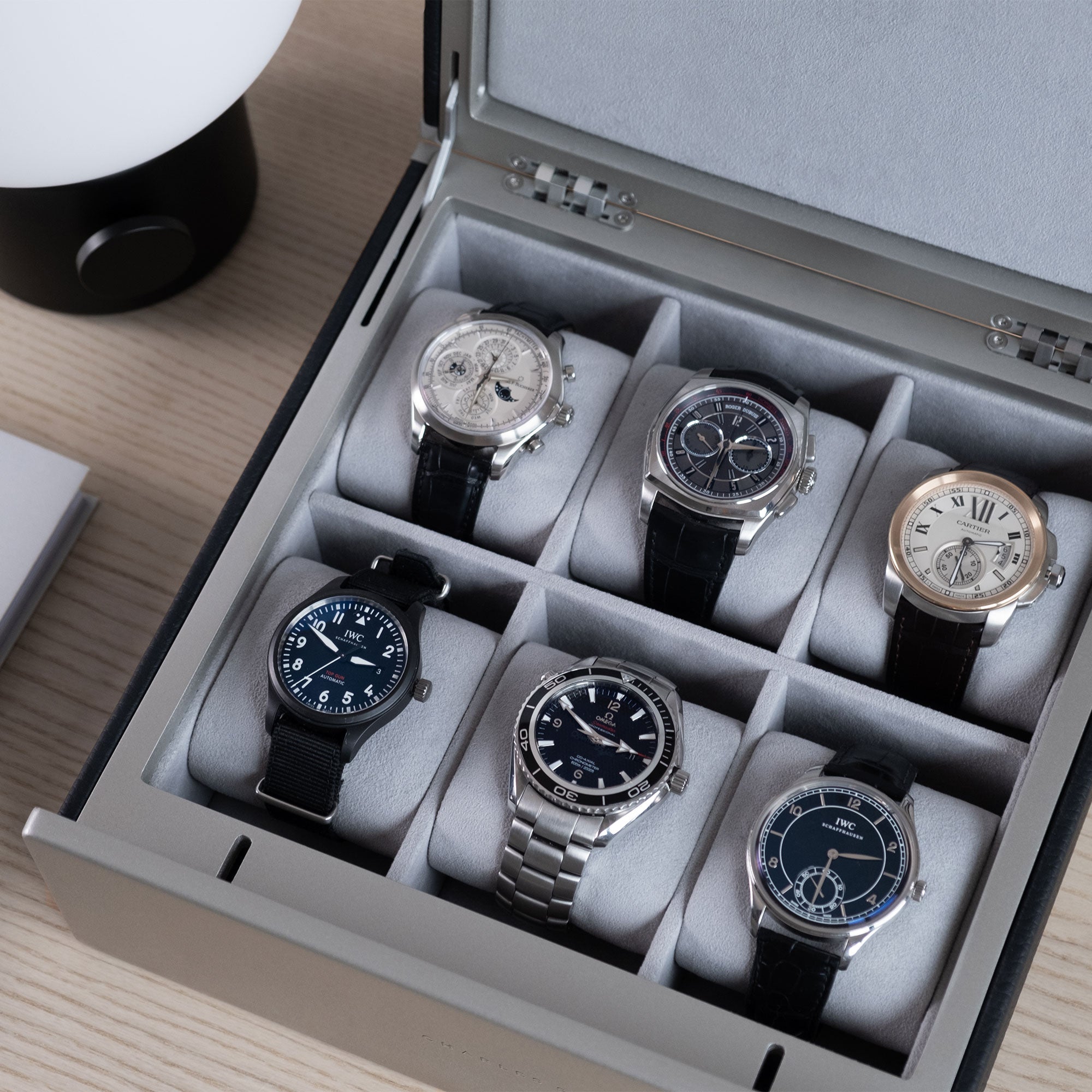 Lifestyle shot of 6 watches placed in Spence watch box. Handmade in Canada from black leather, carbon fiber and anodized aluminum casing and fog grey Alcantara interior