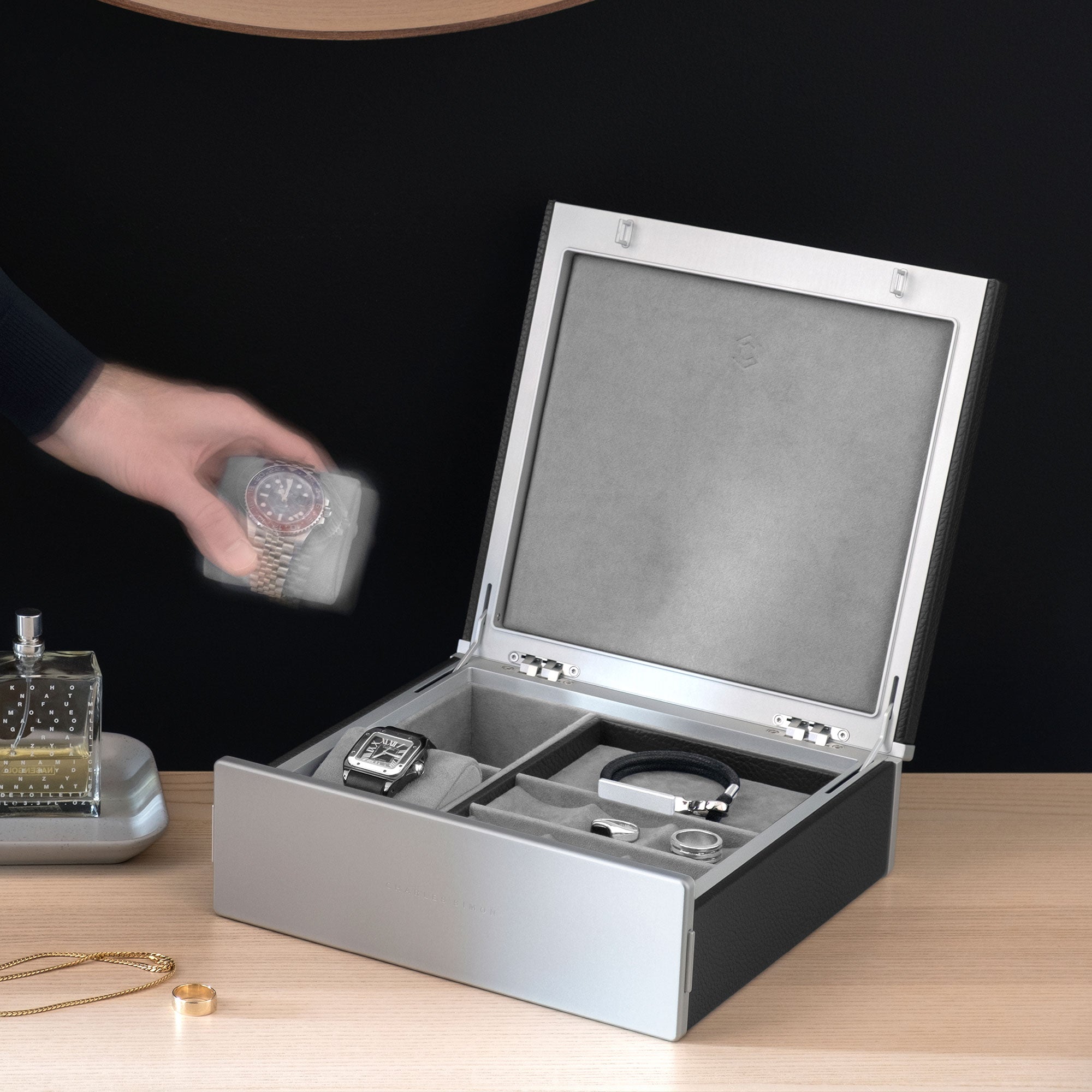 Lifestyle photo of black leather and notte interior Taylor 2 Watch and Jewelry box. Man is taking Rolex watch placed on watch cushion from the watch and jewelry box. The Taylor 2 Watch and Jewelry box holds a black leather bracelet, silver rings and a Cartier watch.