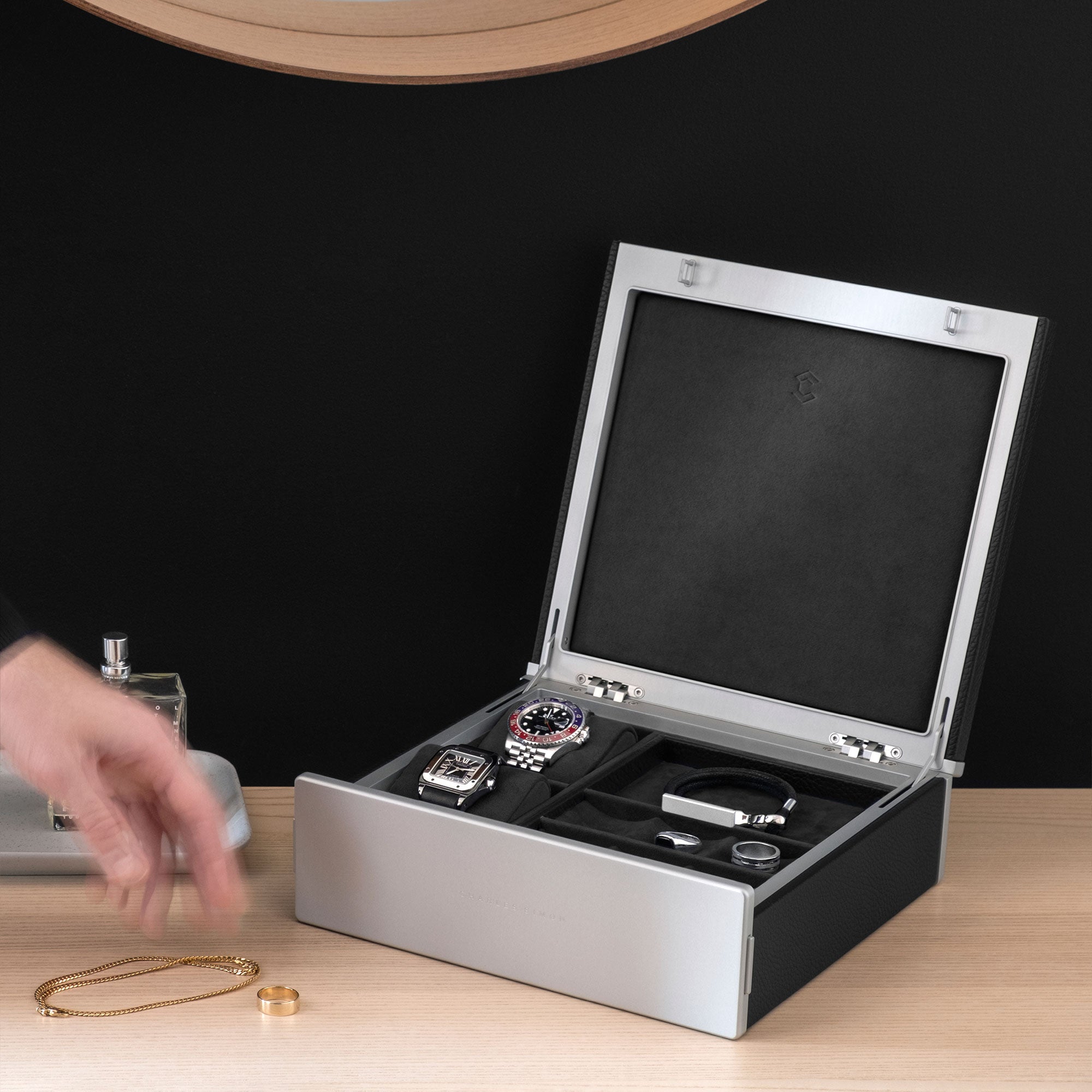 Lifestyle image of open Taylor 2 Watch box in black leather holding 2 luxury watches and a jewelry collection of gold and silver rings, necklaces and bracelets