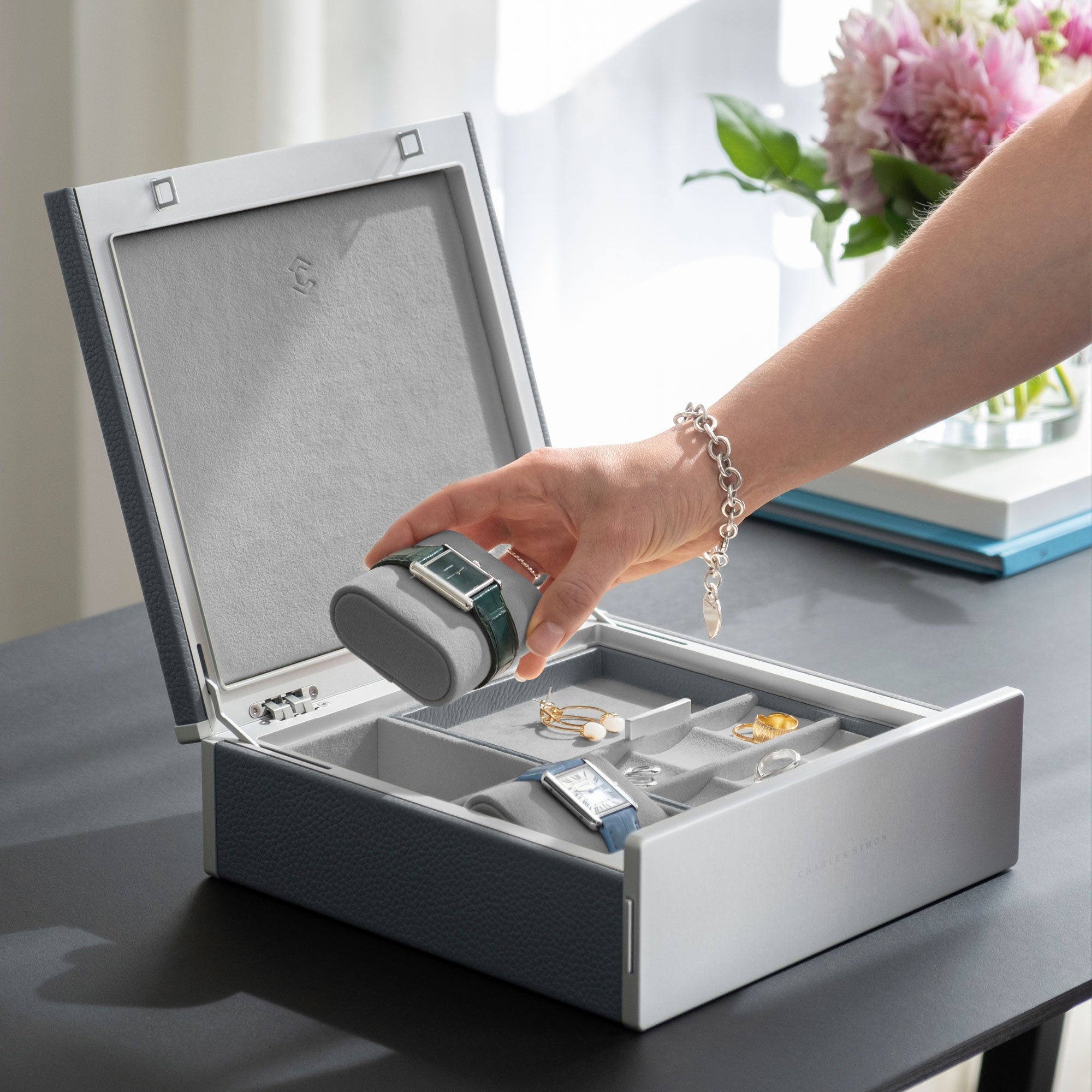 Lifestyle photo of woman wearing Tiffany bracelet grabbing Cartier watch from the Taylor 2 Watch and Jewelry box in cloud grey leather and fog grey interior