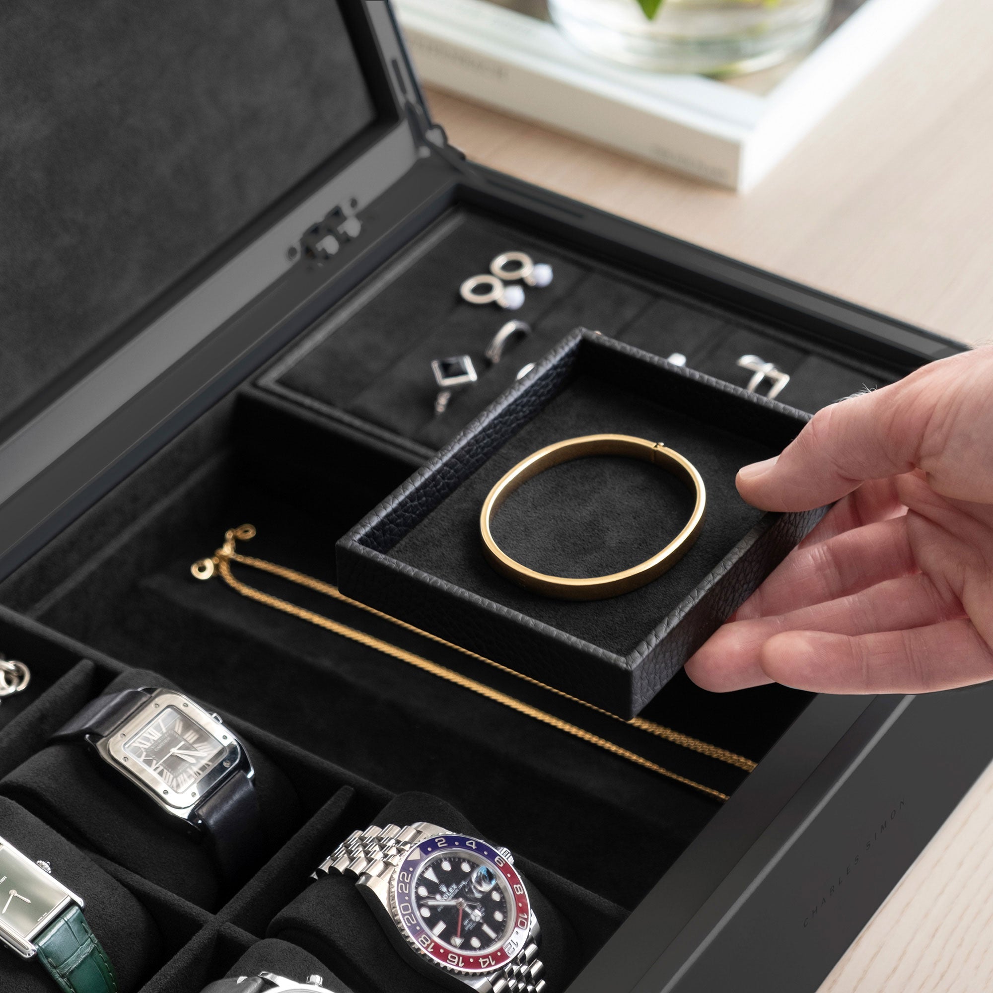 Detail photo of man holding mobile jewelry tray containing a gold bracelet from the all black Taylor 4 Watch and Jewelry box. The Taylor 4 Watch and Jewelry box is storing 4 luxury watches and a collection of fine jewelry, including silver rings, earrings, bracelets and necklaces. 