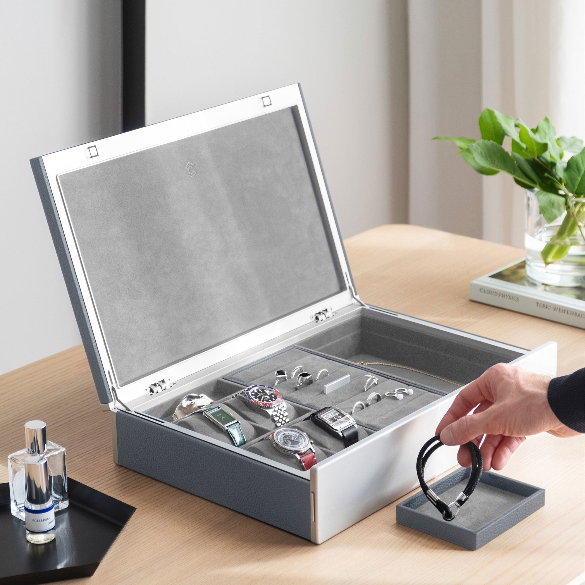 Lifestyle photo of man grabbing leather bracelet from the Taylor 4 Watch and Jewelry box in cloud grey leather and fog grey interior. The Taylor 4 is holding four luxury watches as well as a collection of rings, earrings and other jewelry