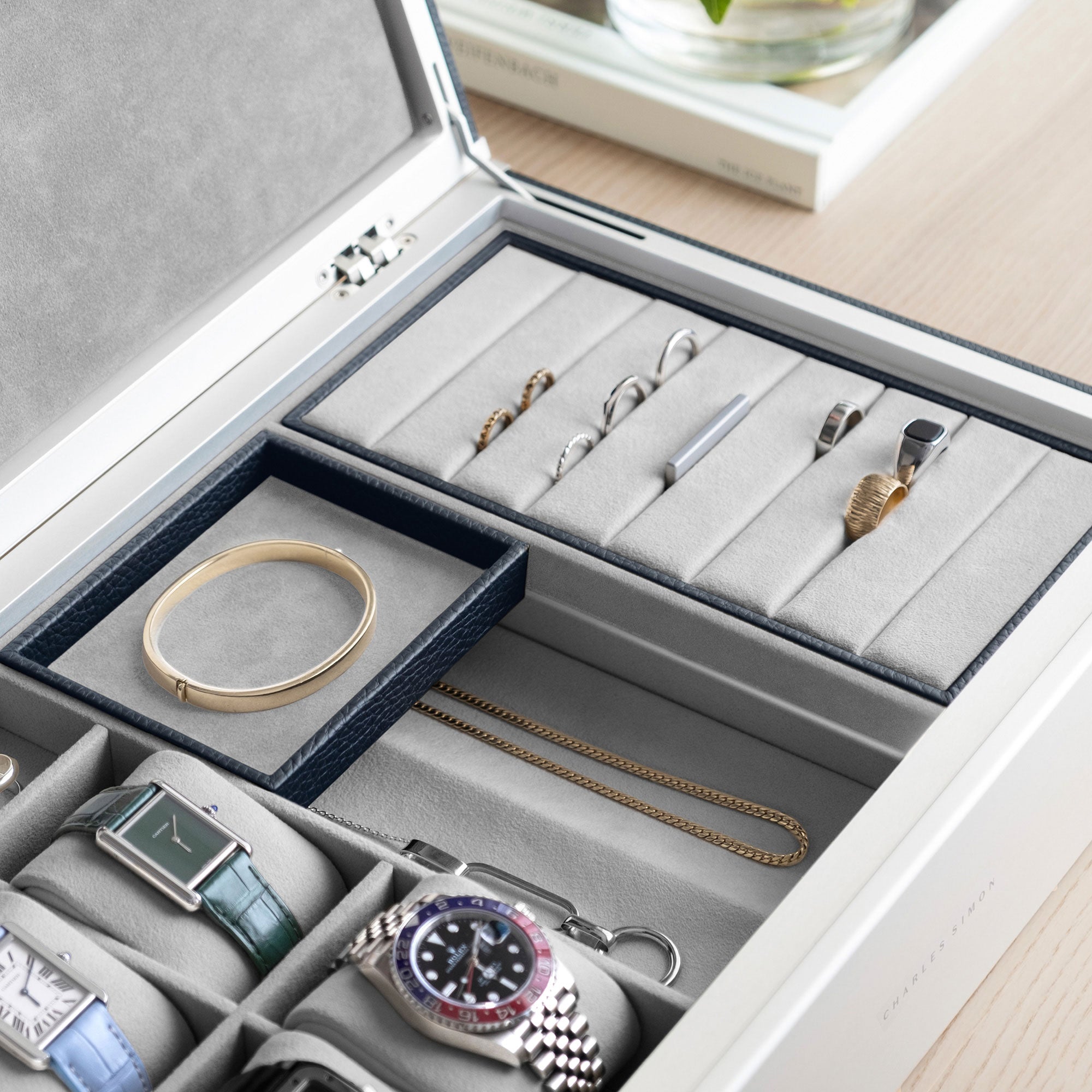 Detail photo of man holding mobile jewelry tray containing a gold bracelet from the marine leather and fog grey interior Taylor 4 Watch and Jewelry box. The Taylor 4 Watch and Jewelry box is storing 4 luxury watches and a collection of fine jewelry, including gold and silver rings, earrings, bracelets and necklaces.