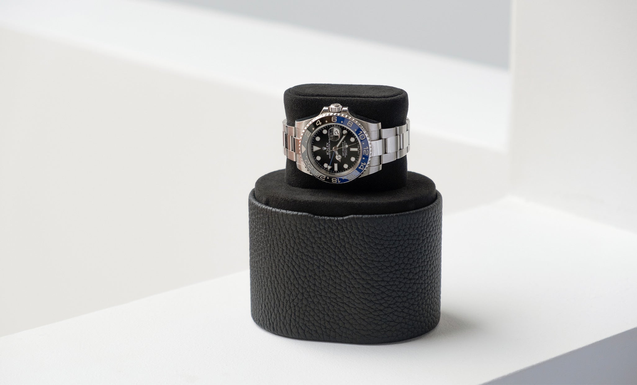 Minimalist Theo Watch roll in black leather and black Alcantara with a Batman Rolex watch placed on it . The Watch roll serves as a convenient way to transport your watch while traveling and quickly transforms into a convenient watch stand 