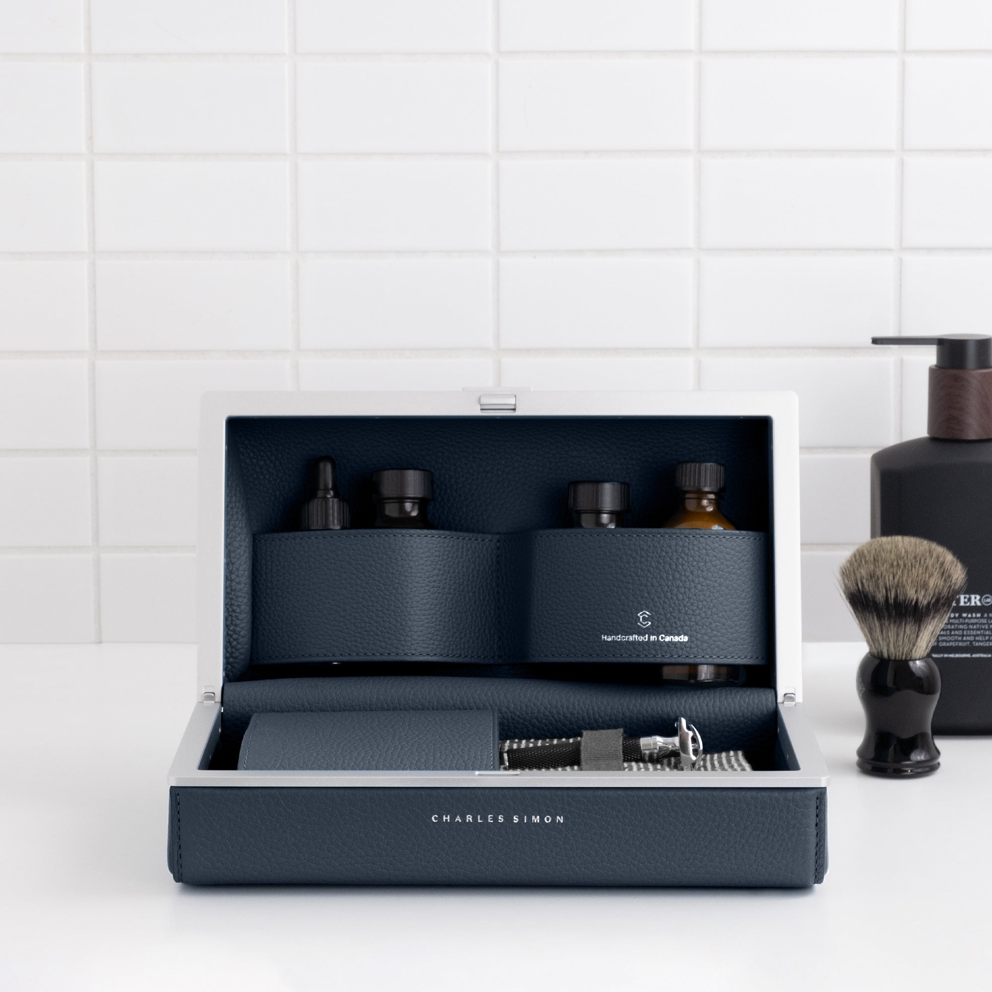 Lifestyle photo of open marine leather Moraine Toiletry bag holding makeup, skincare and other bathroom essentials.