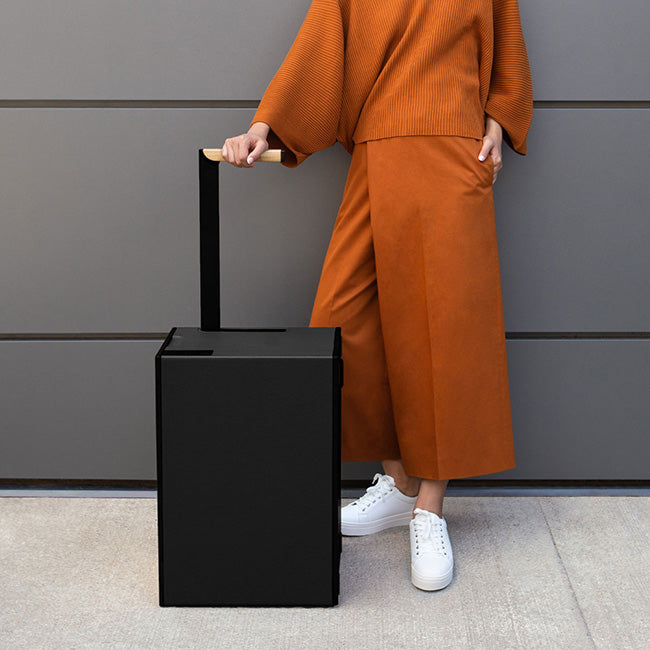 luxury rolling luggage in black, minimalist design luggage, Bonaventure by Charles Simon, girl standing next to the rolling luggage
