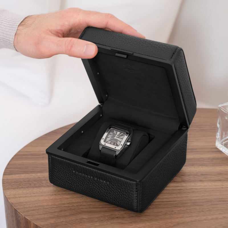 Lifestyle photo of all black Eaton 1 watch case on modern nightstand. Man is opening luxury watch case with Cartier Santos placed on Notte removable watch cushion. 