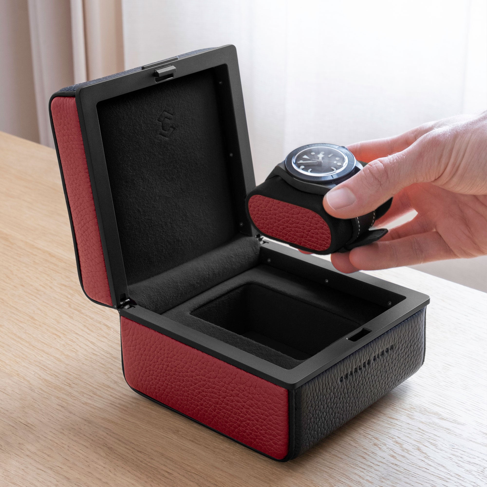 Lifestyle photo of Eaton 1 watch case in black and contrasting red leather. Man is opening luxury watch case with Tagheuer watch placed on Notte and red leather removable watch cushion.