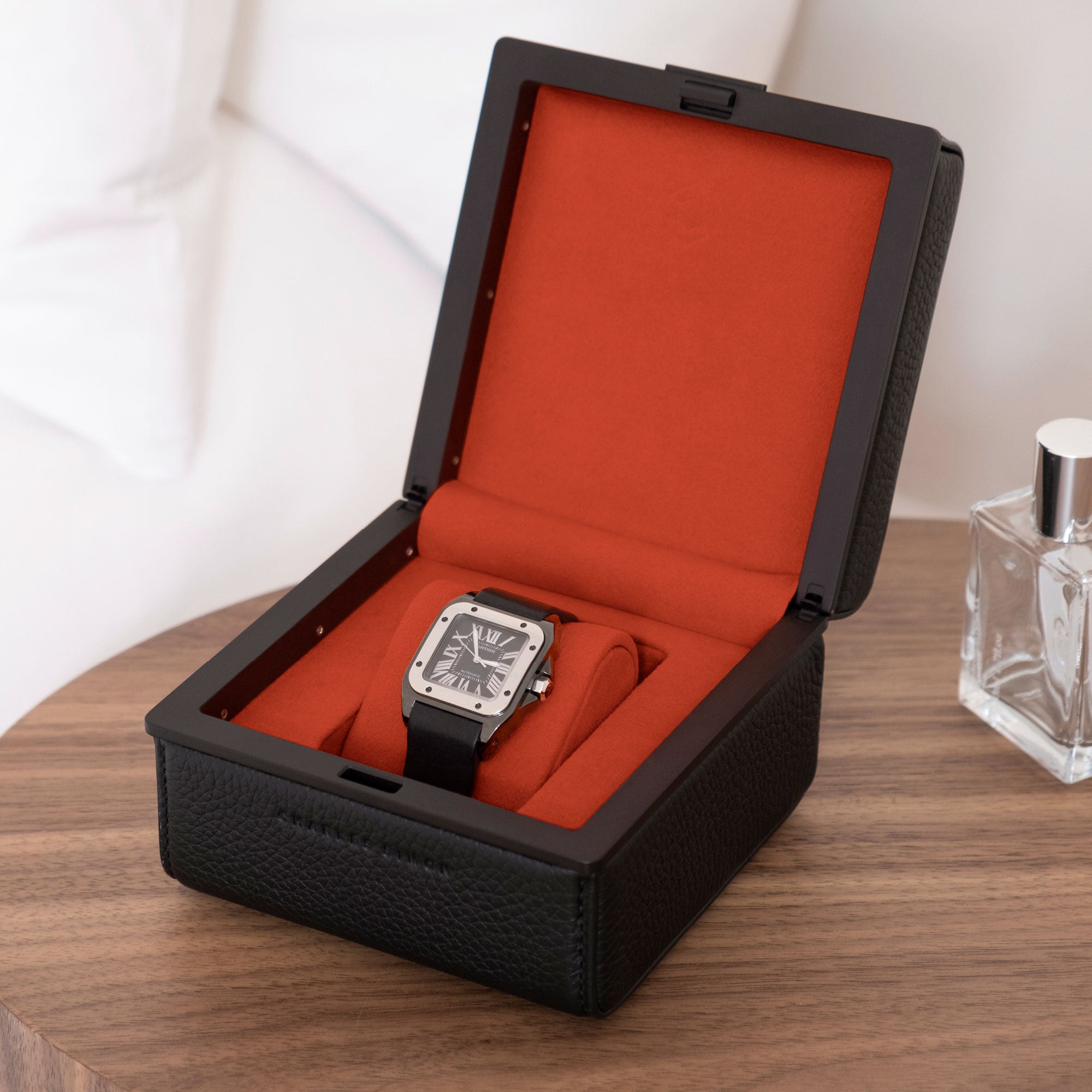 Lifestyle photo of black leather Eaton 1 luxury watch case displaying a Cartier Santos watch on its Vermilion watch cushion.