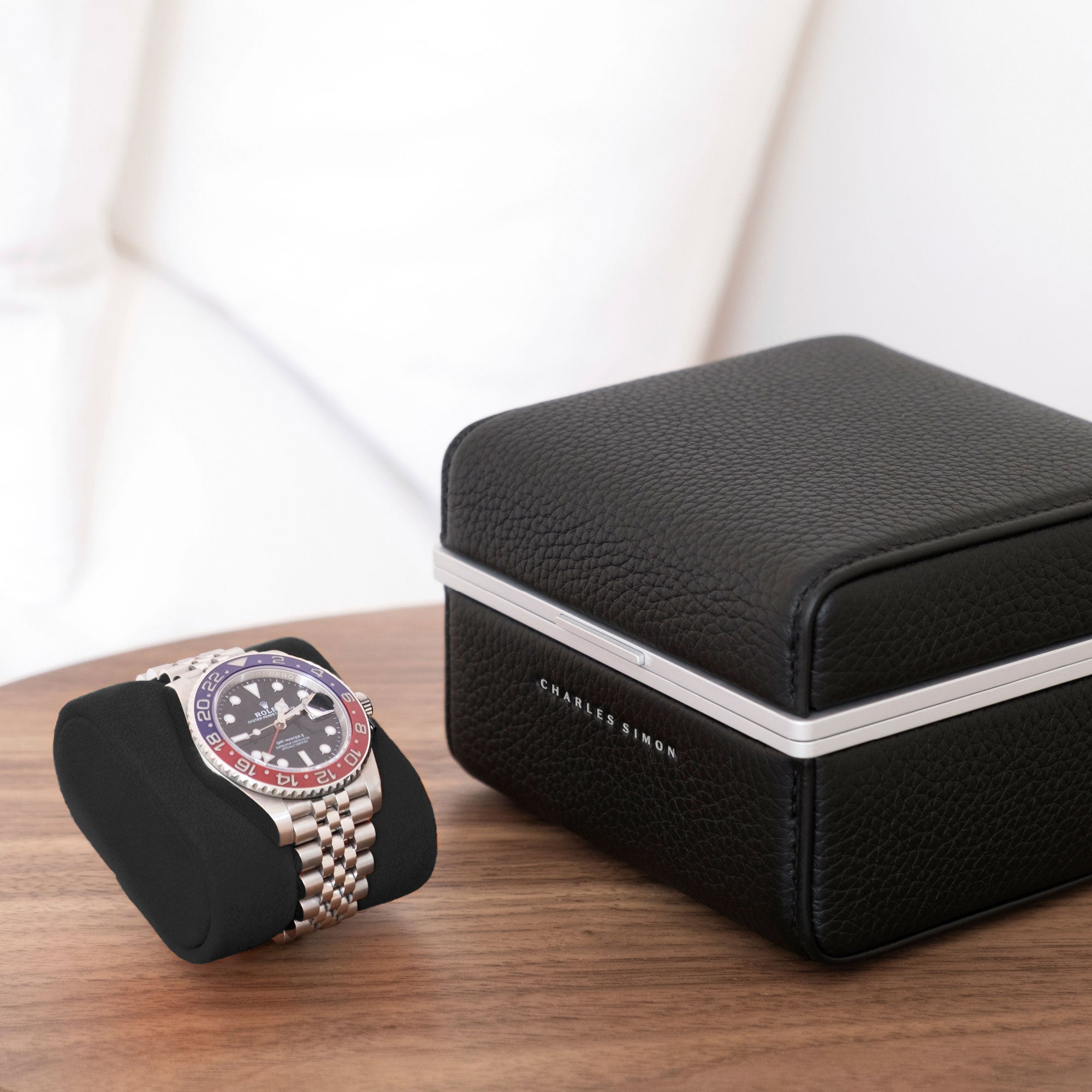 Lifestyle photo of Rolex watch placed on Alcantara cushion next to closed Eaton 1 watch case in black leather and grey anodized aluminum