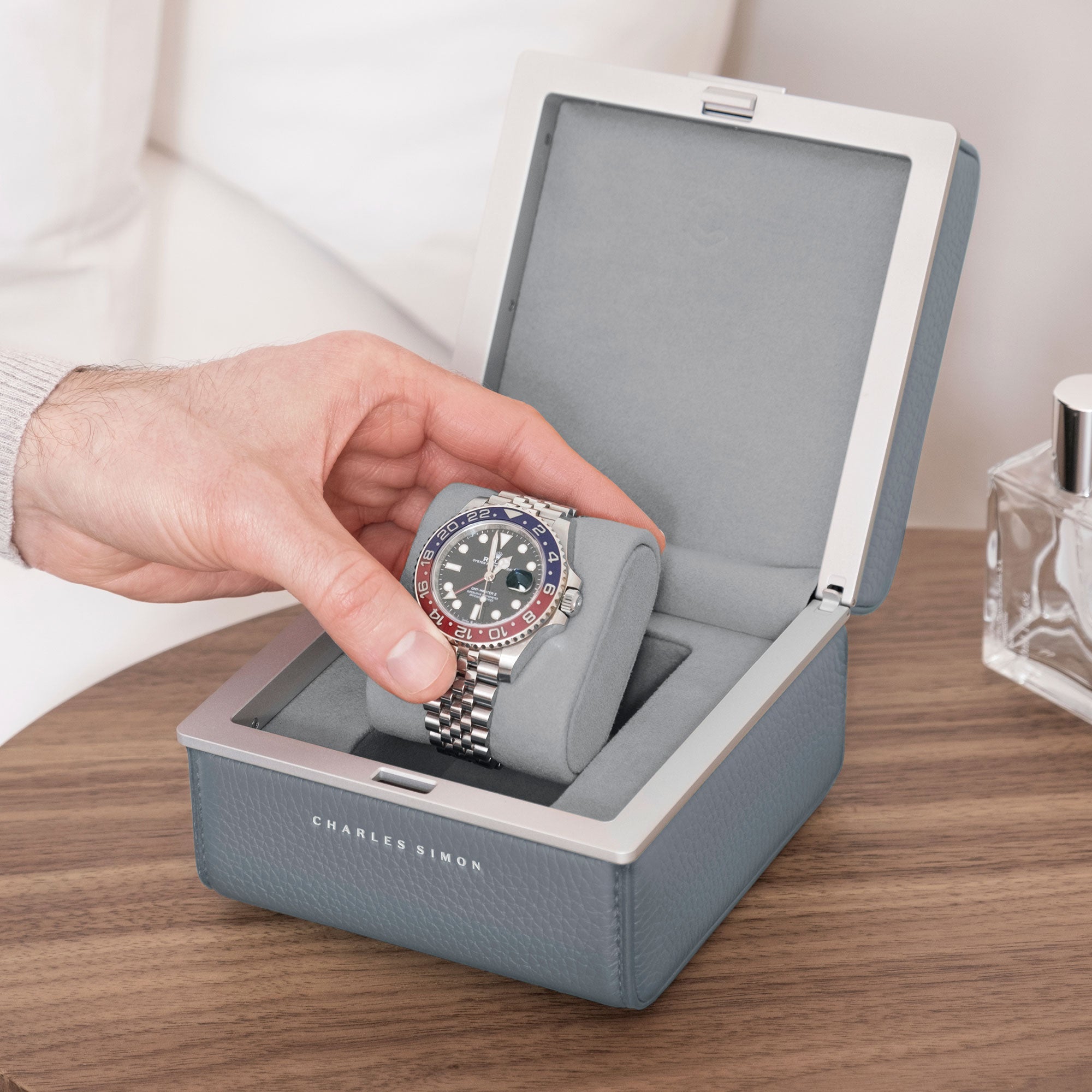 Lifestyle photo of cloud grey Eaton 1 watch case on modern nightstand. Man is opening luxury watch case with Rolex Pepsi placed on fog grey removable watch cushion.