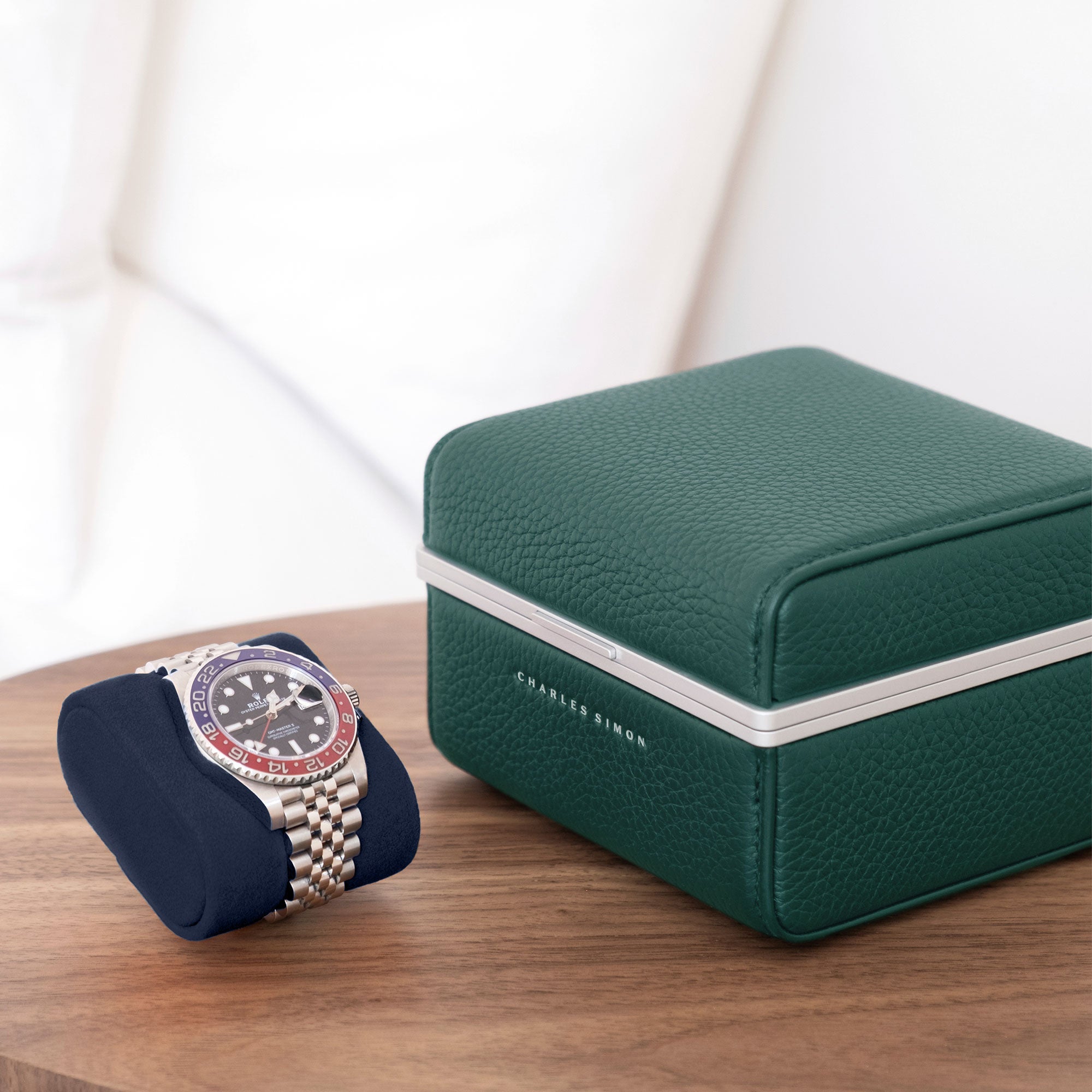 Lifestyle photo of all emerald Eaton 1 Watch case sitting closed on minimalist table. Rolex Pepsi luxury watch is placed on deep blue removable Alcantara cushion next to closed luxury watch case
