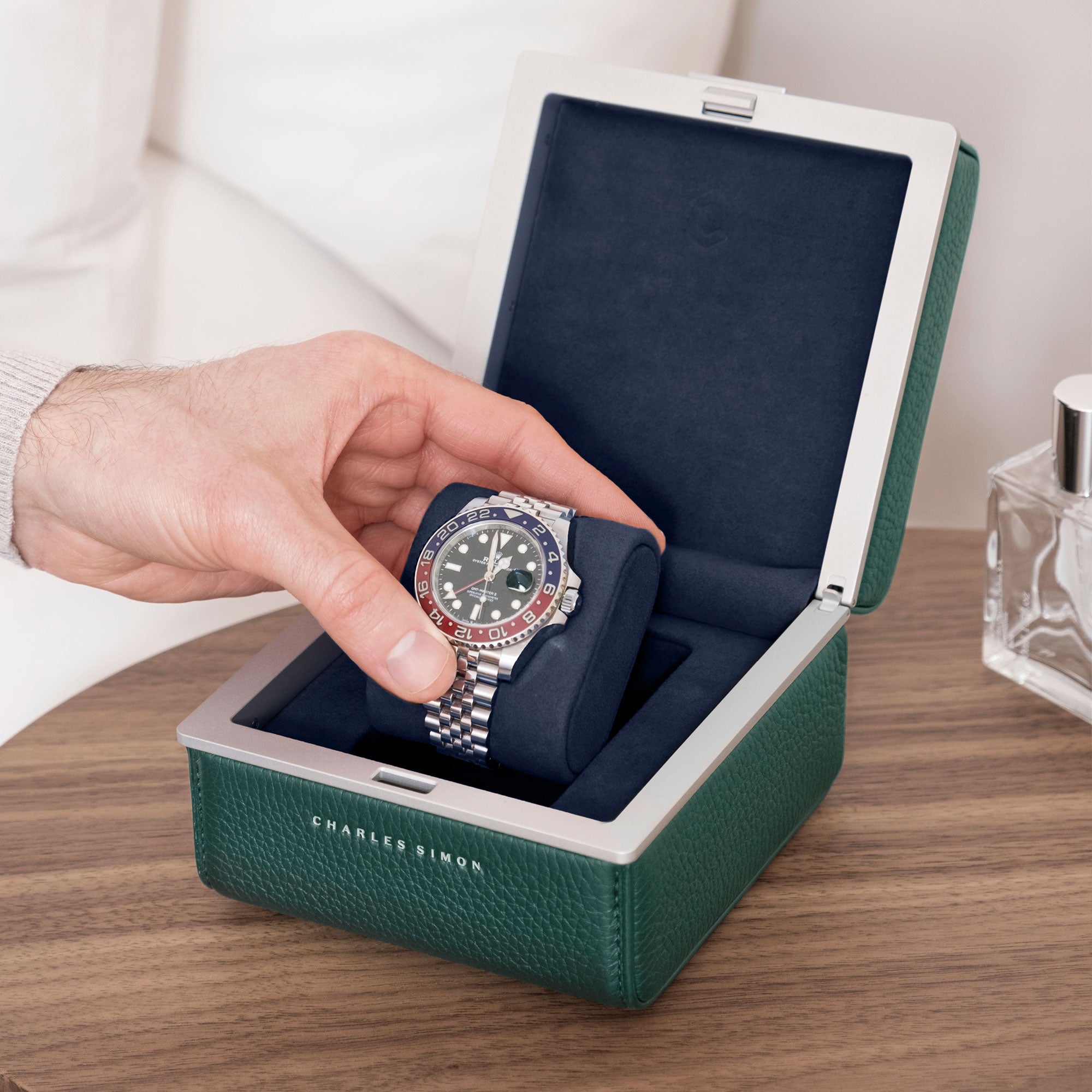 Lifestyle photo of emerald Eaton 1 watch case on modern nightstand. Man is opening luxury watch case with Rolex Pepsi watch placed on deep blue removable watch cushion.
