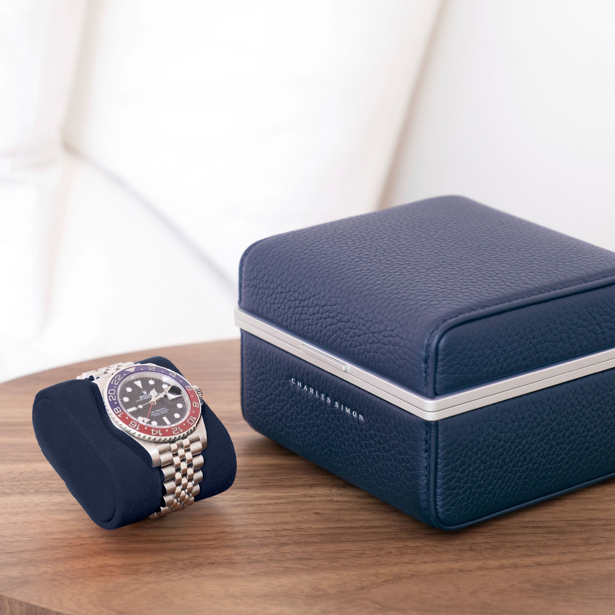 Lifestyle photo of sapphire Eaton 1 Watch case sitting closed on minimalist table. Rolex Pepsi luxury watch is placed on deep blue removable Alcantara cushion next to closed luxury watch case