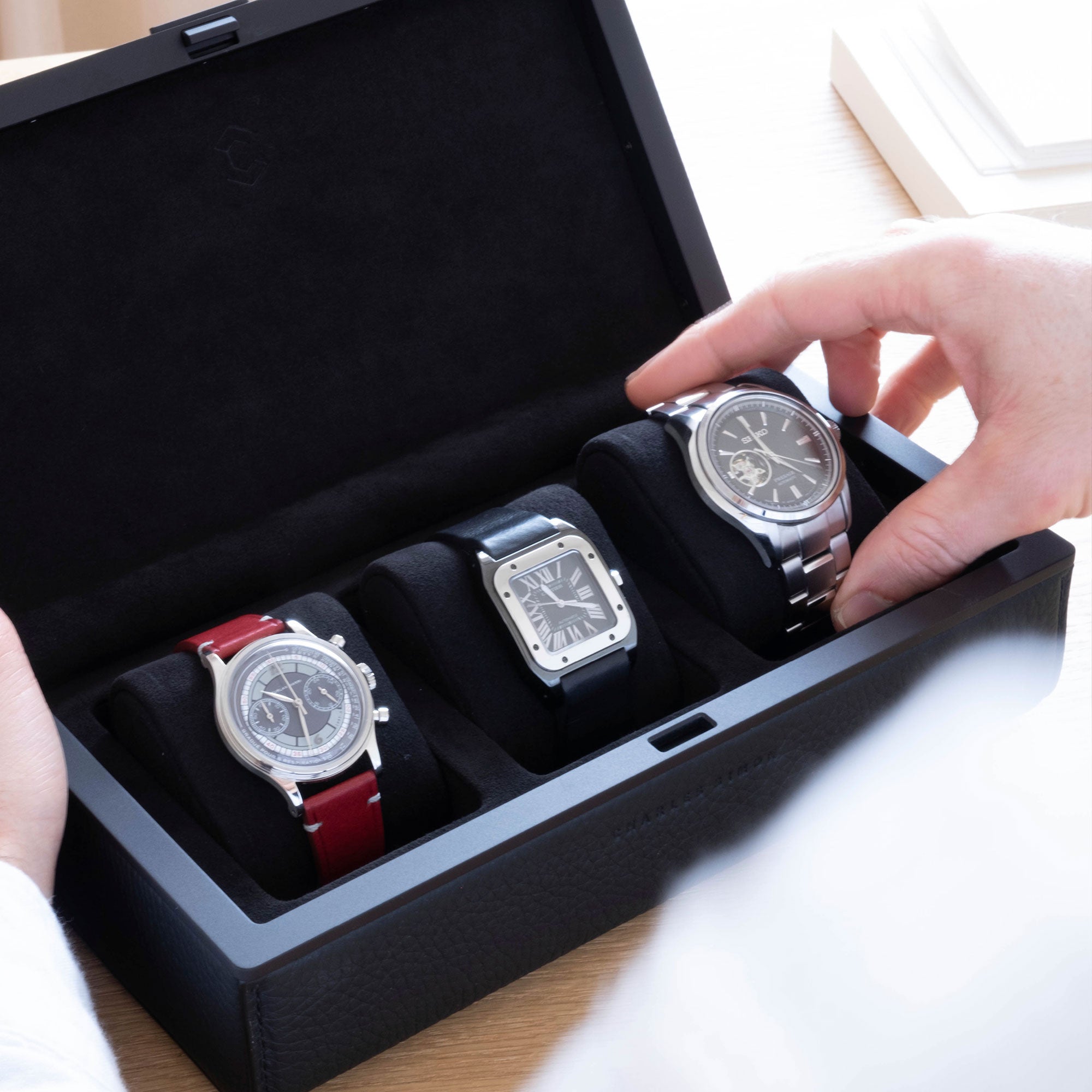 Lifestyle shot of Eaton 3 luxury watch case for 3 watches holding collection of 3 watches, including Furlan Marri, Cartier and Seiko placed on removable Alcantara watch cushions.