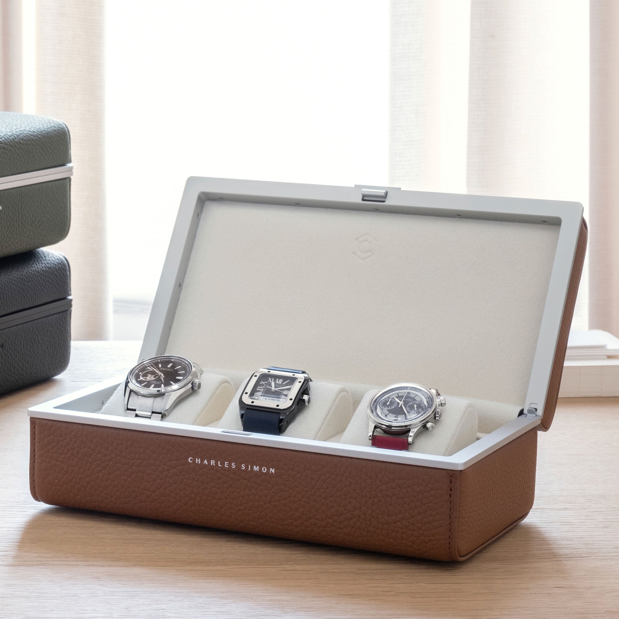 Lifestyle photo of open Eaton 3 Watch case in tan leather and eggshell interior displaying 3 luxury watches