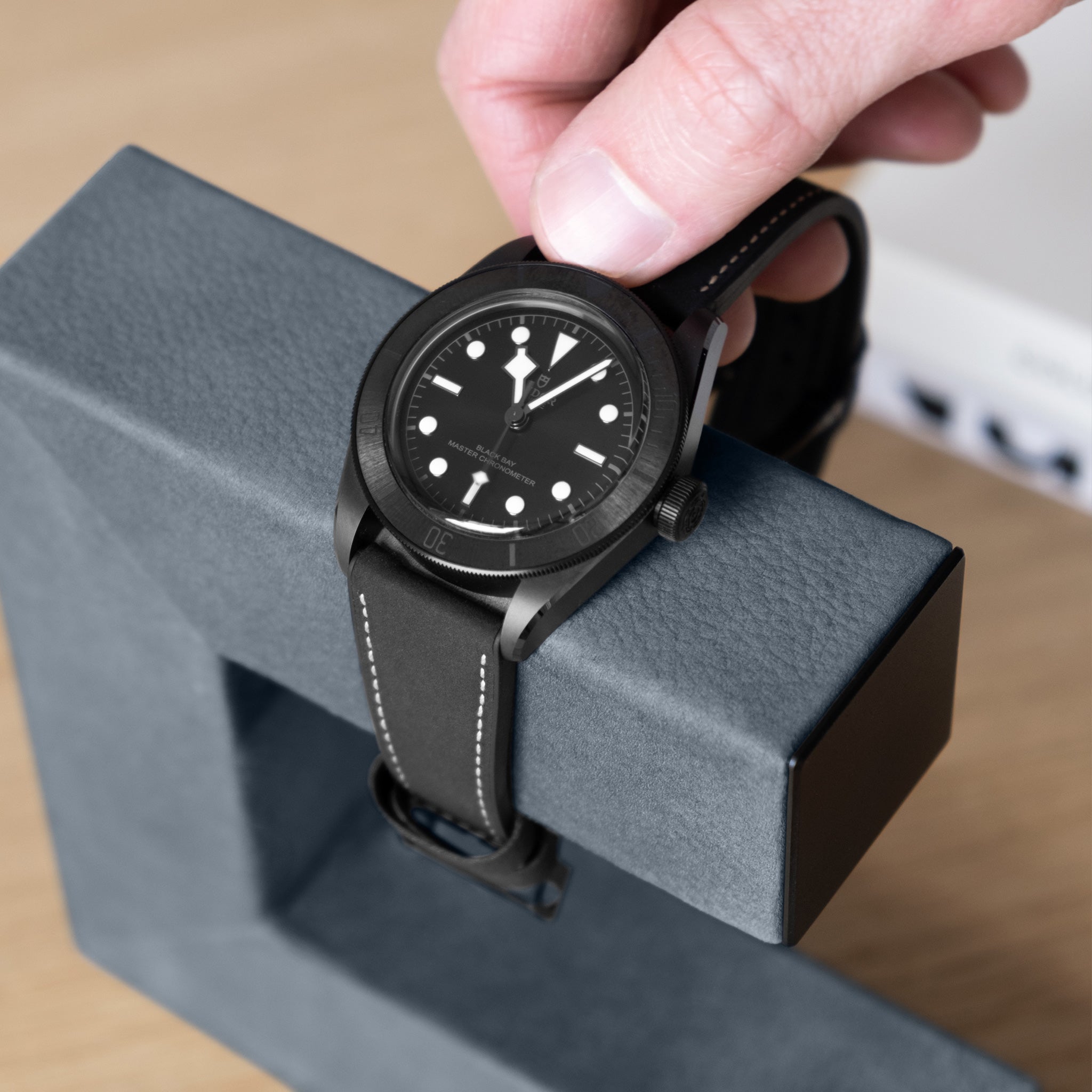 Men's watch being taken from luxury watch stand in dusty blue nubuck leather and black anodized aluminum.