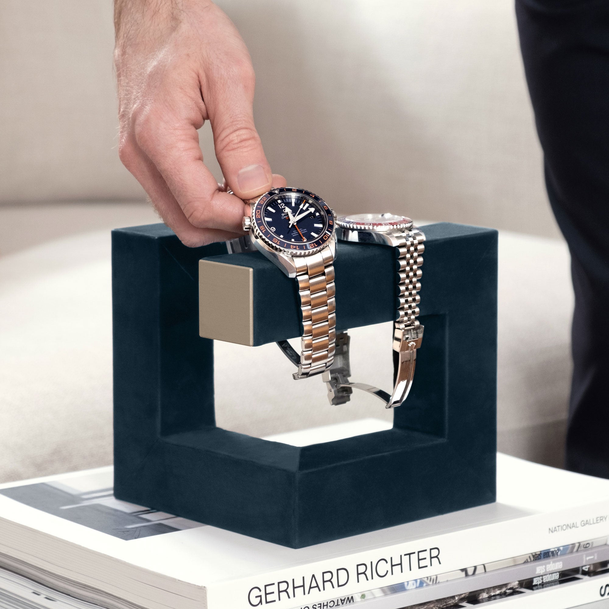 Lifestyle photo of man taking his watch from his navy-teal and gold watch stand