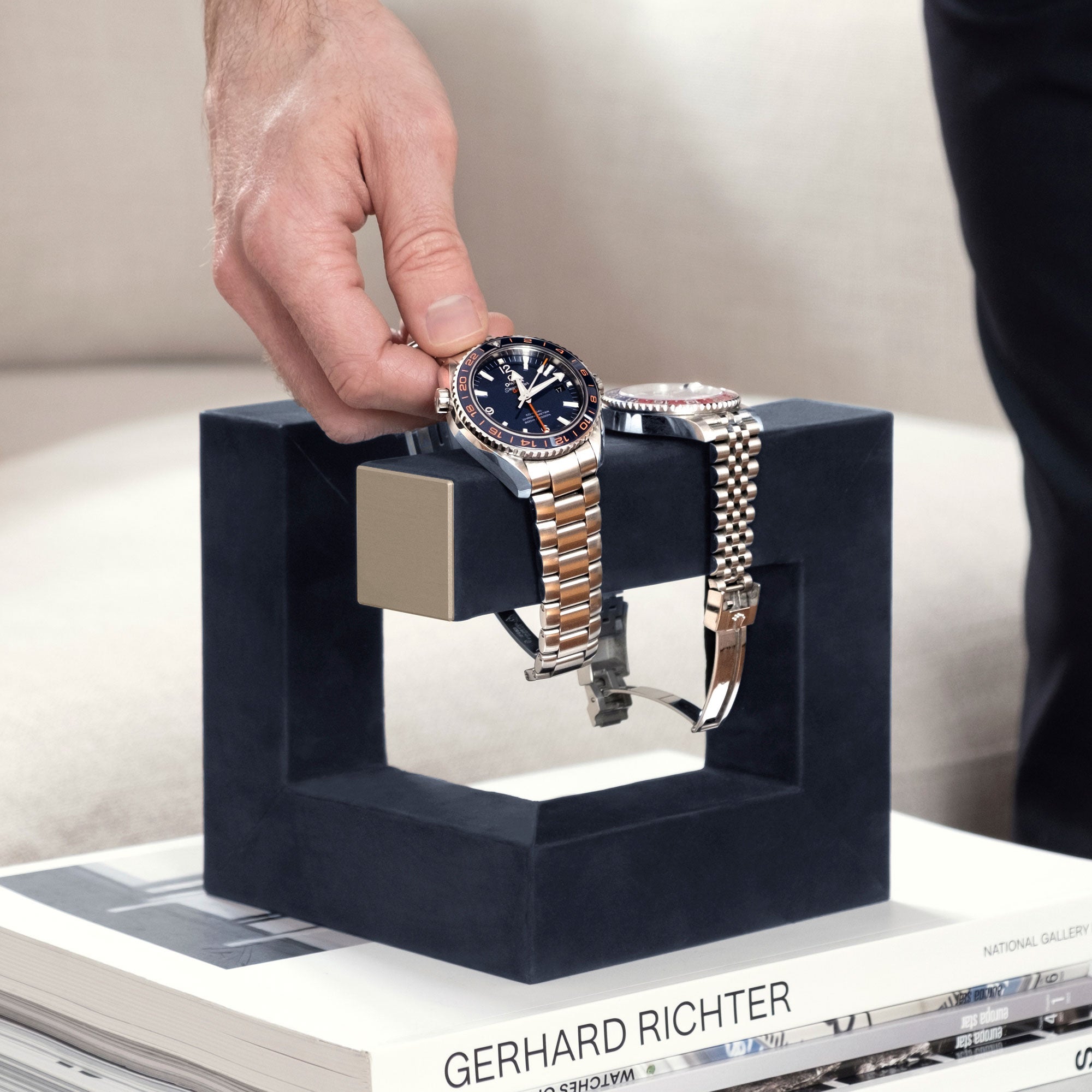 Lifestyle photo of man taking his watch from his navy and gold watch stand