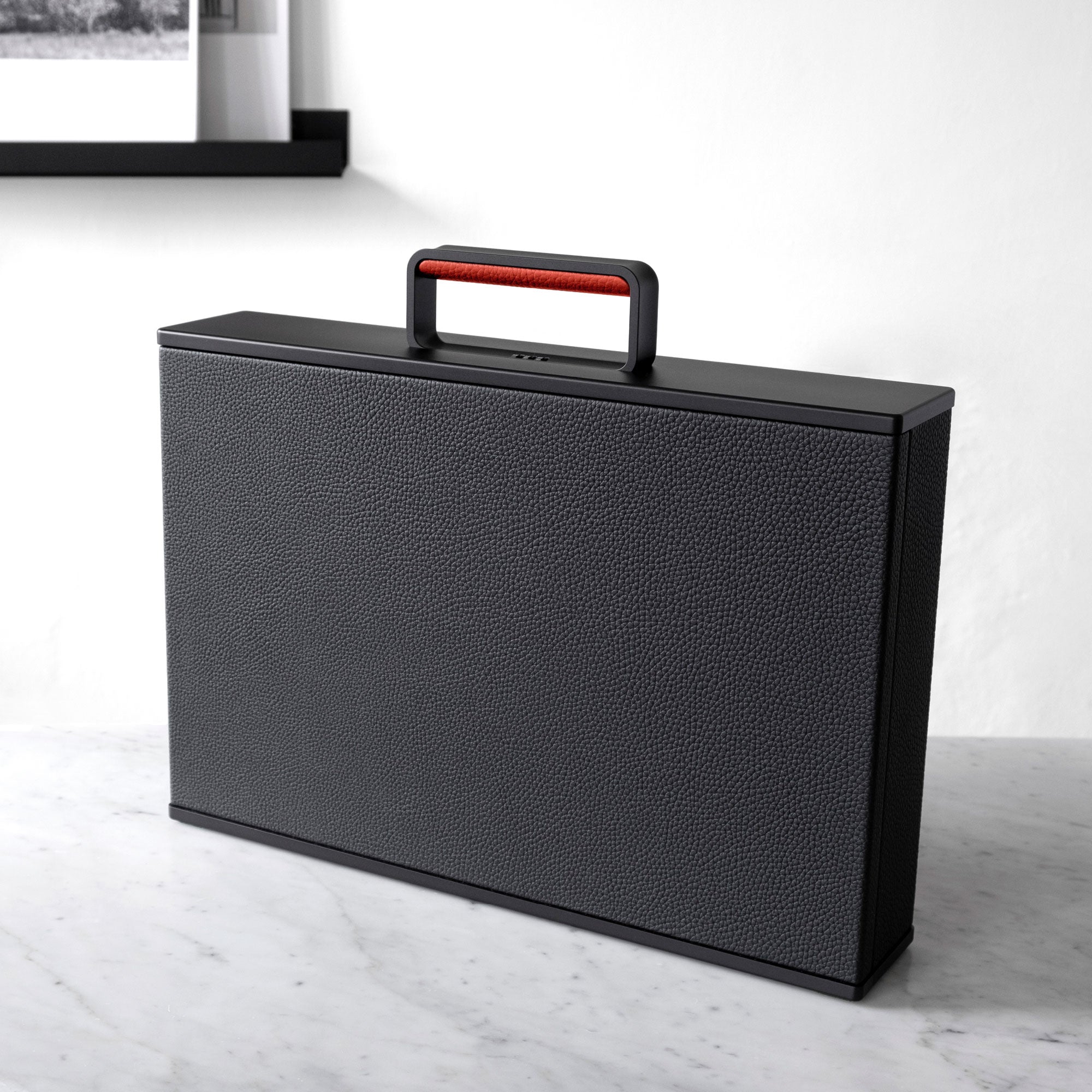 Lifestyle photo of 3/4 view of the boldly minimalist black and red Mackenzie briefcase. This luxurious briefcase transports all your work essentials in style. 